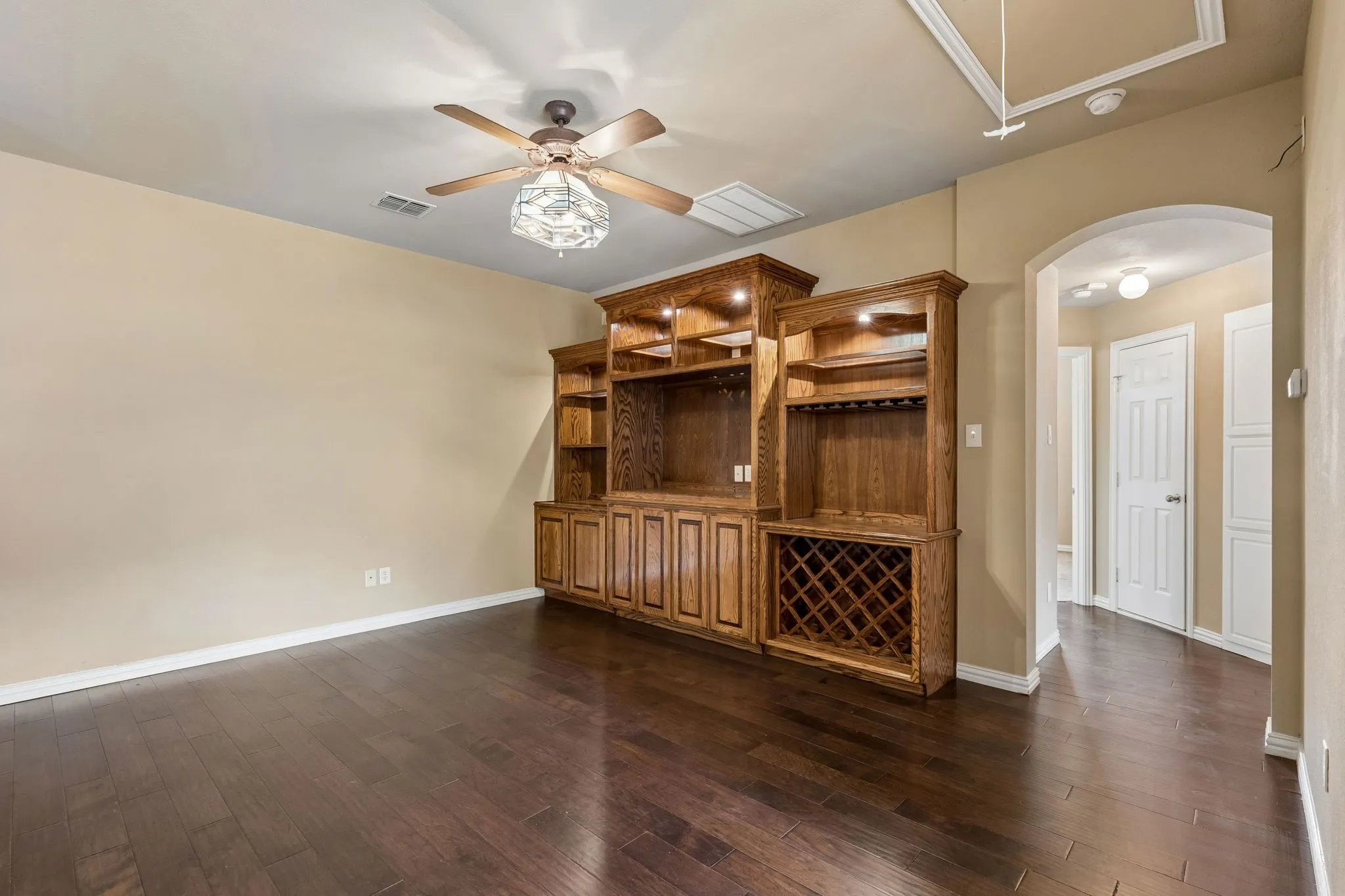 Wood-finish flooring throughout, custom built-in cabinetry with integrated lighting and wine storage, decorative ceiling fan, and arched doorway