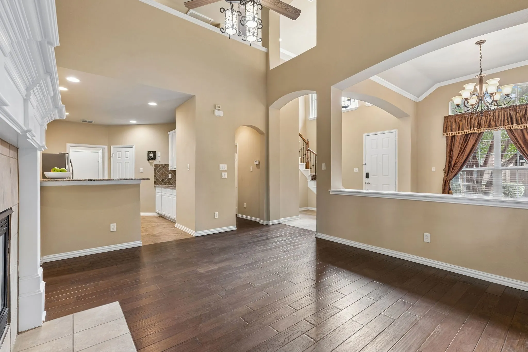 Vaulted ceilings, wood-finish flooring, arched doorways, white fireplace surround, and recessed lighting