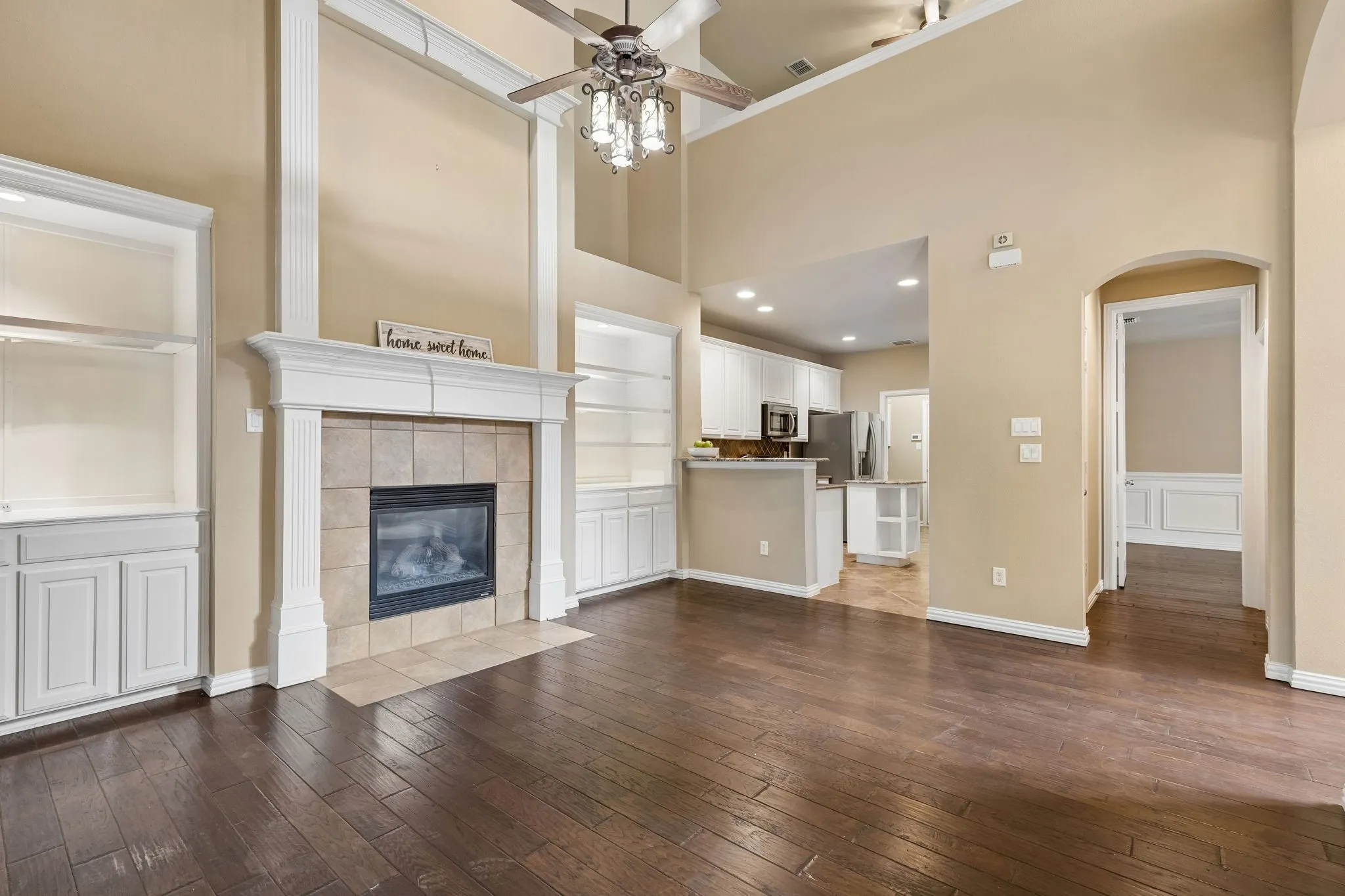 Spacious living area featuring high ceilings, a tiled fireplace with mantel, built-in shelving, and dark wood-finish flooring. Breakfast bar to kitchen