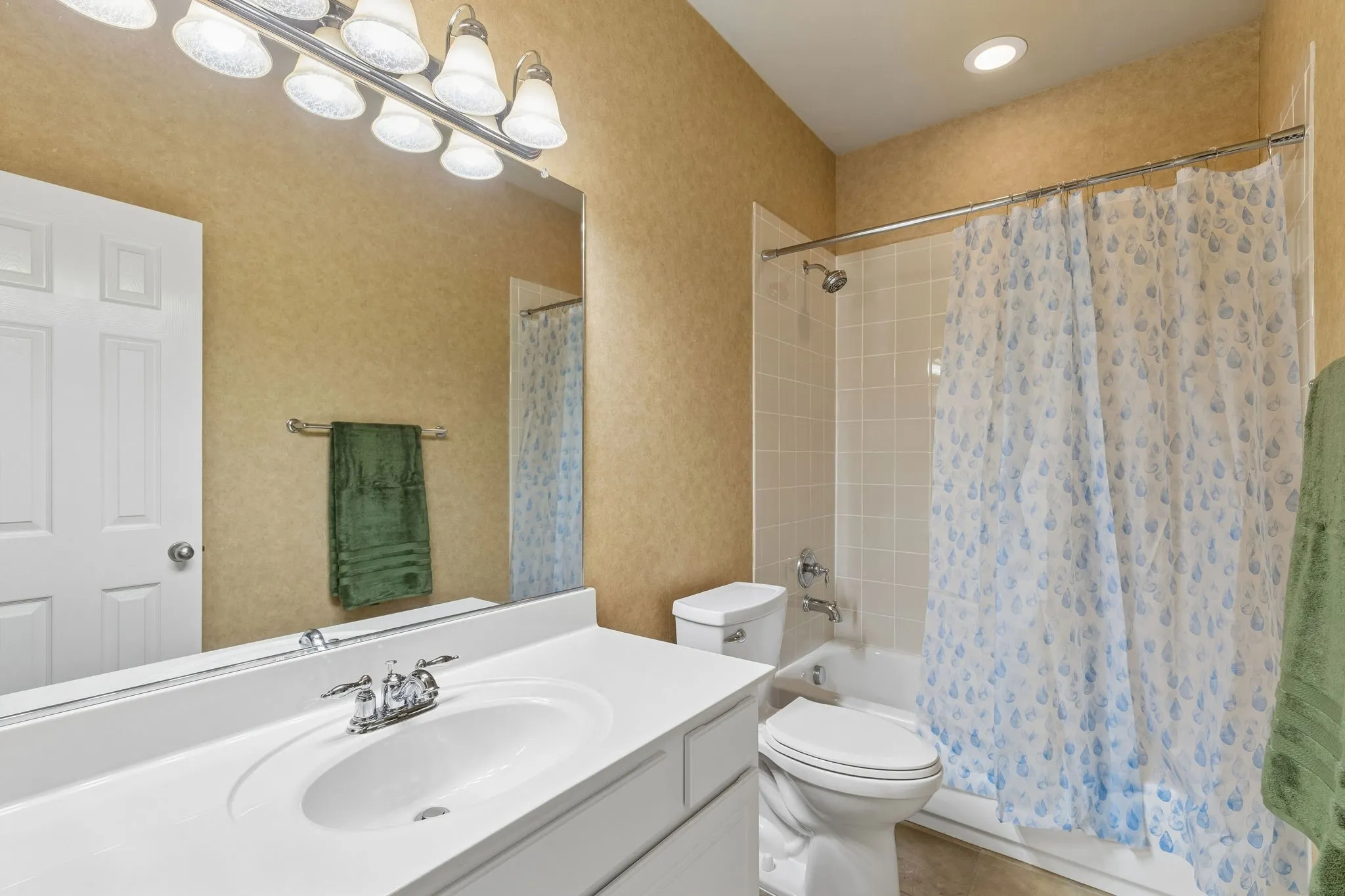 Bathroom featuring a vanity with an integrated sink, polished chrome faucet, and a large mirror with multi-bulb lighting, tub and shower
