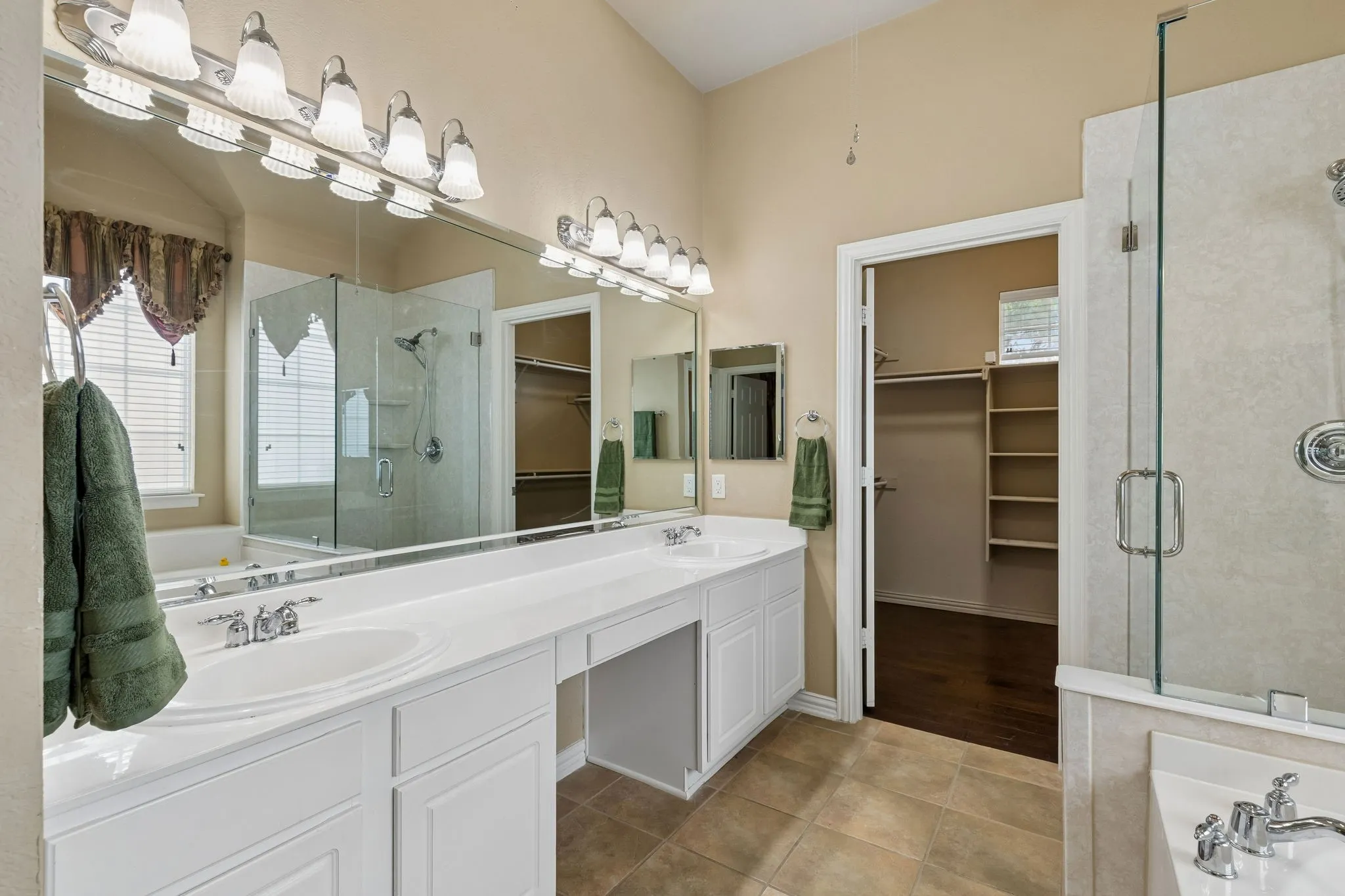 Dual vanities with integrated sinks, extensive countertop space, glass-enclosed shower, large built-in bathtub, and large walk-in closet