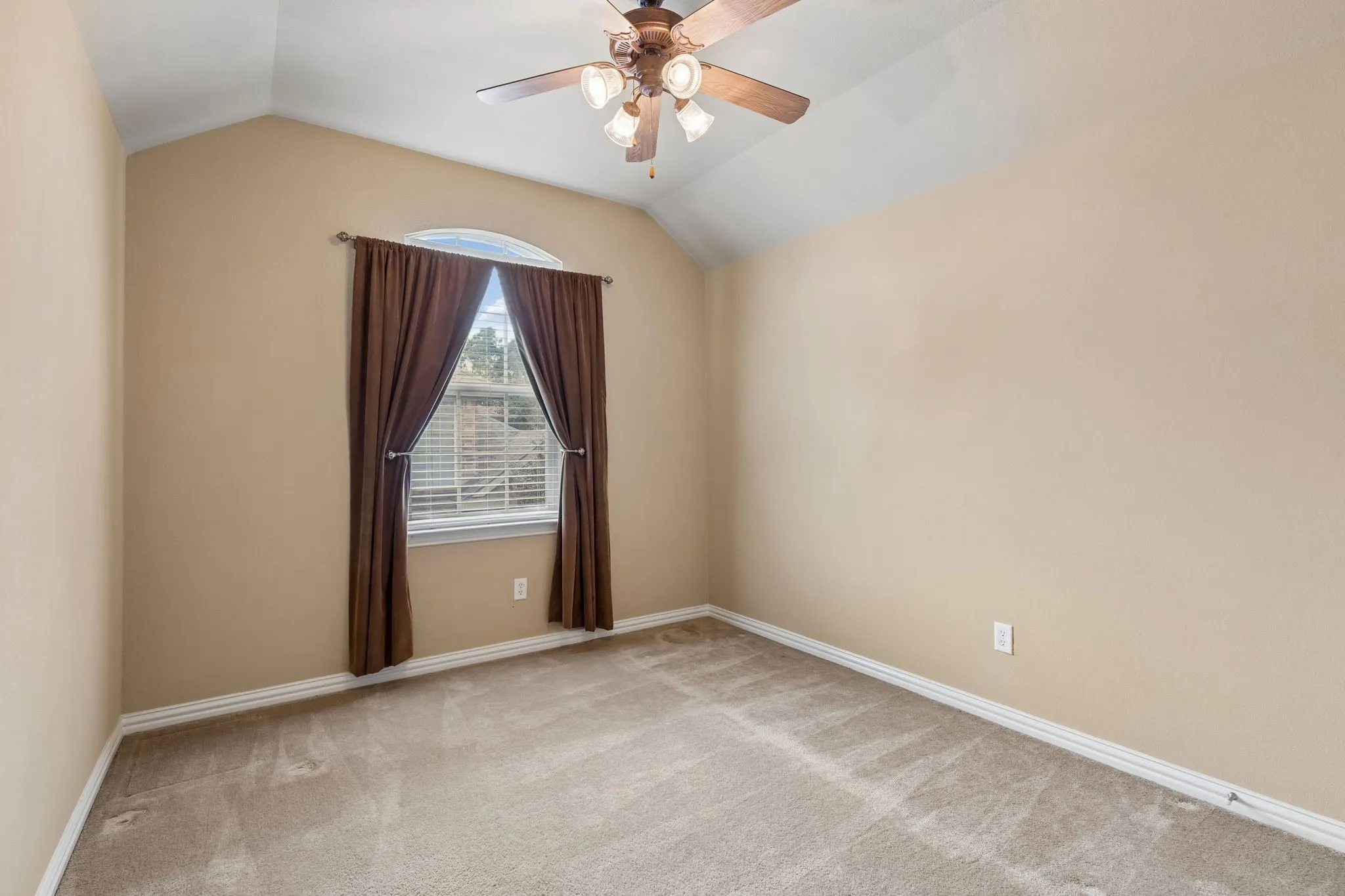 Vaulted ceiling, ceiling fan, arched transom window, window with blinds, and neutral carpet