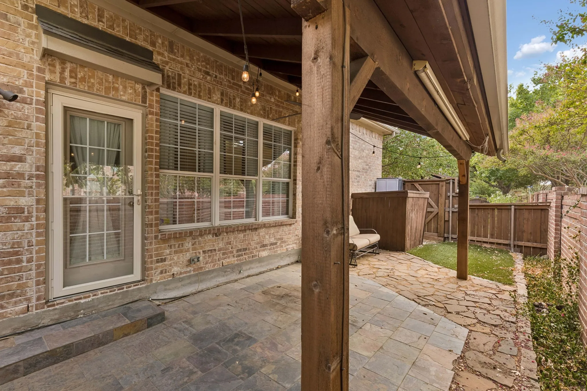 Covered patio with stone paver flooring, brick exterior, and wood pergola structure