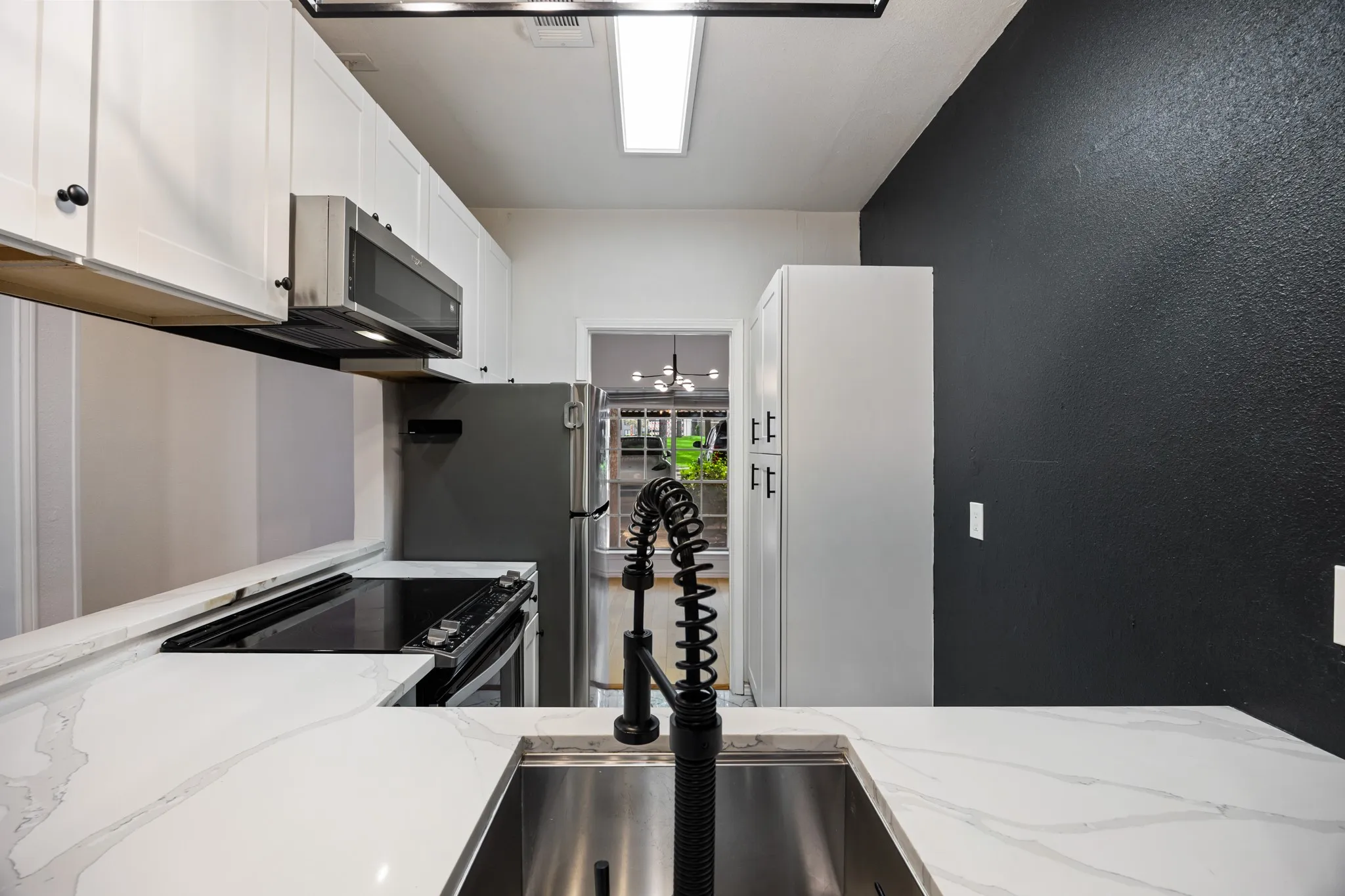 White shaker-style cabinetry with dark hardware, stainless steel appliances, white patterned countertops, stainless steel undermount sink, and a black gooseneck pull-down faucet