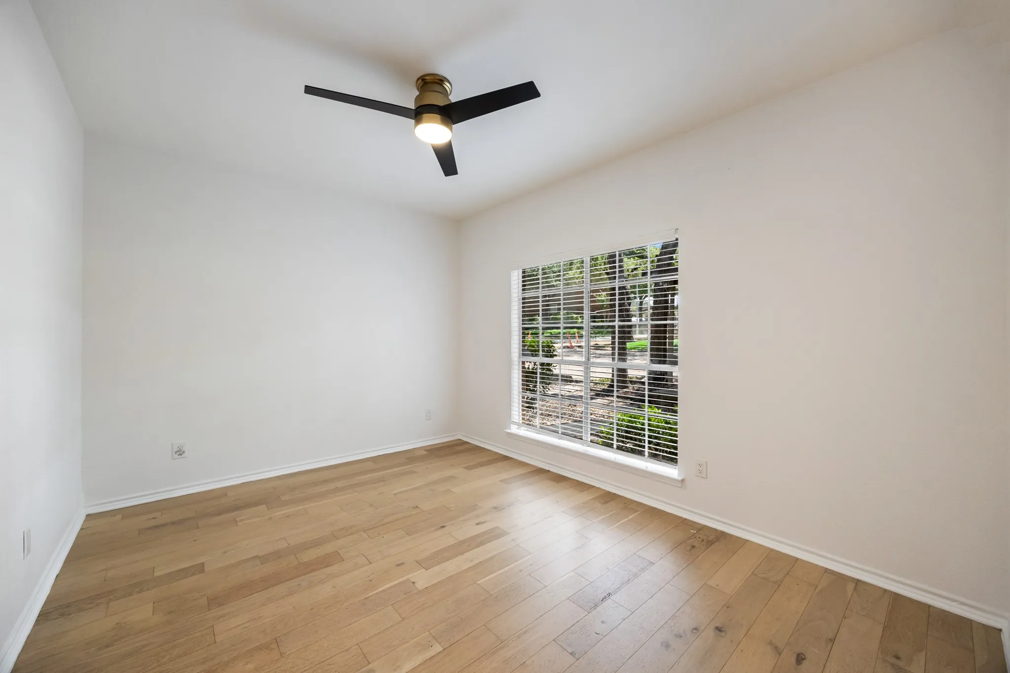 Light wood-finish flooring, white walls, and a modern ceiling fan with integrated lighting