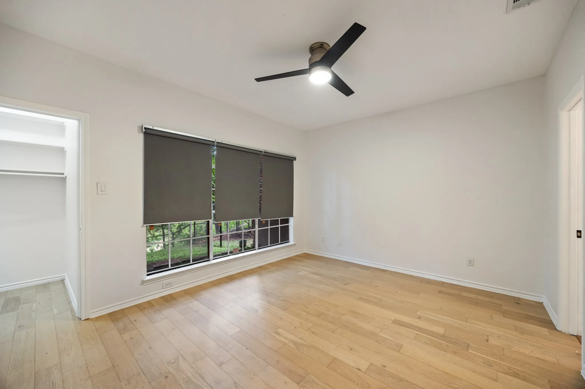 Light wood-finish flooring, a contemporary ceiling fan, and a built-in closet with shelving