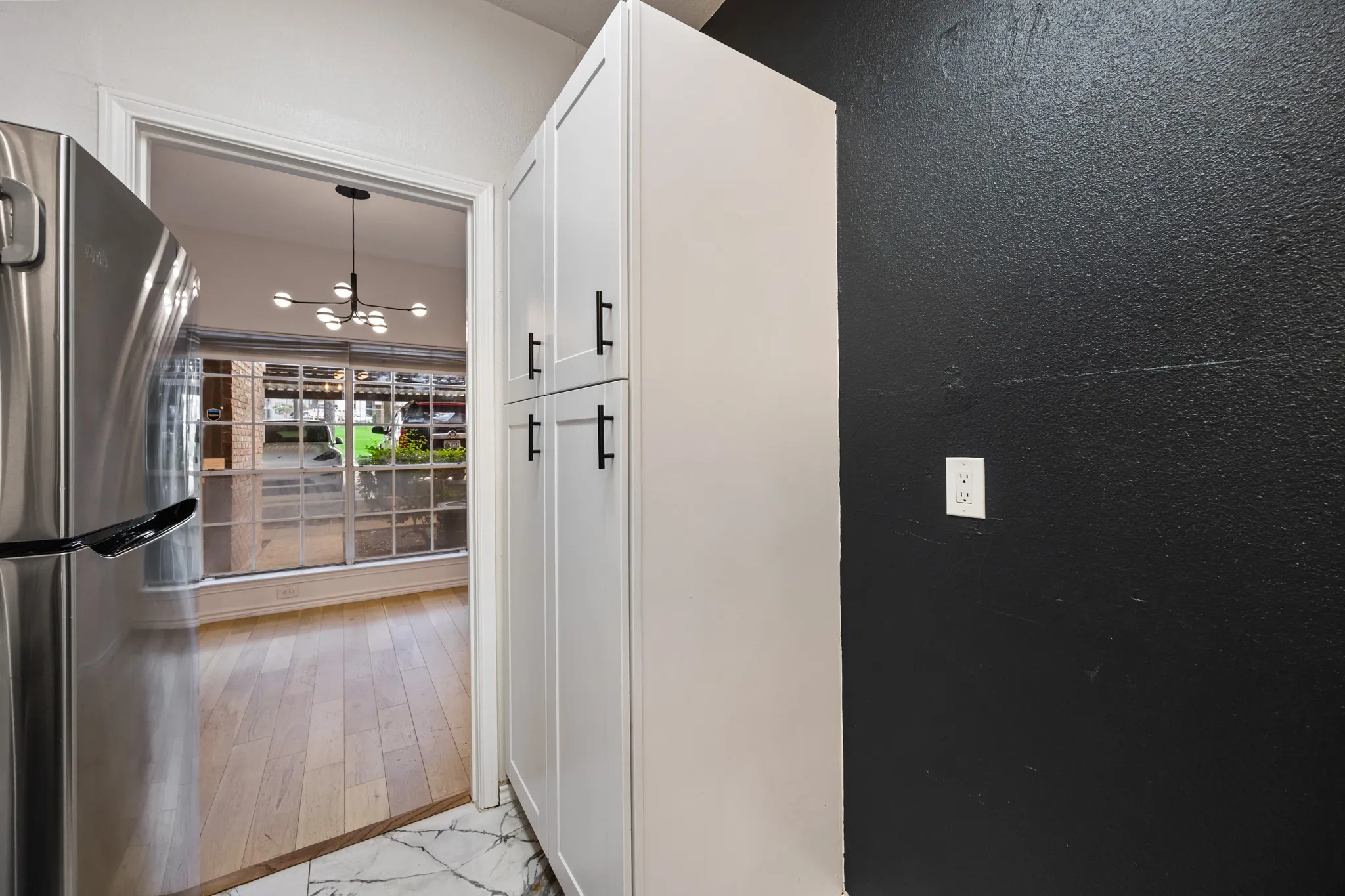 Stainless steel refrigerator, white shaker-style cabinetry with black hardware, and patterned floor tile