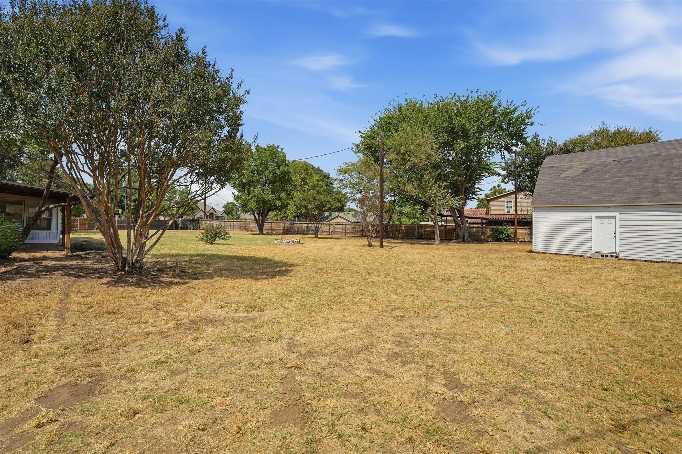 Expansive backyard featuring mature trees, a detached storage building with a shingled roof, and a privacy fence