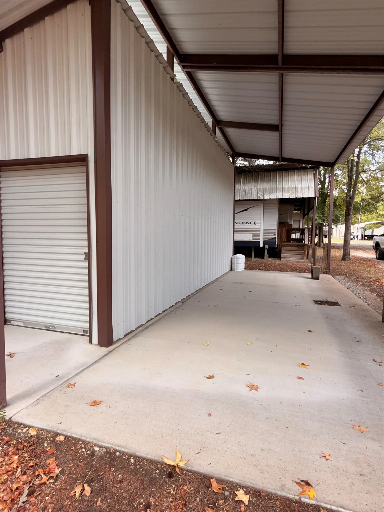 Metal-sided structure featuring a roll-up door, covered concrete pad, and an extended metal roof awning