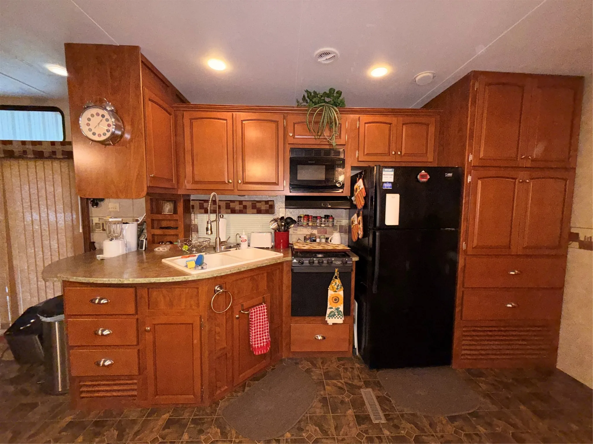 U-shaped kitchen with wood-finish cabinetry, solid surface countertops, a built-in microwave, and a black refrigerator