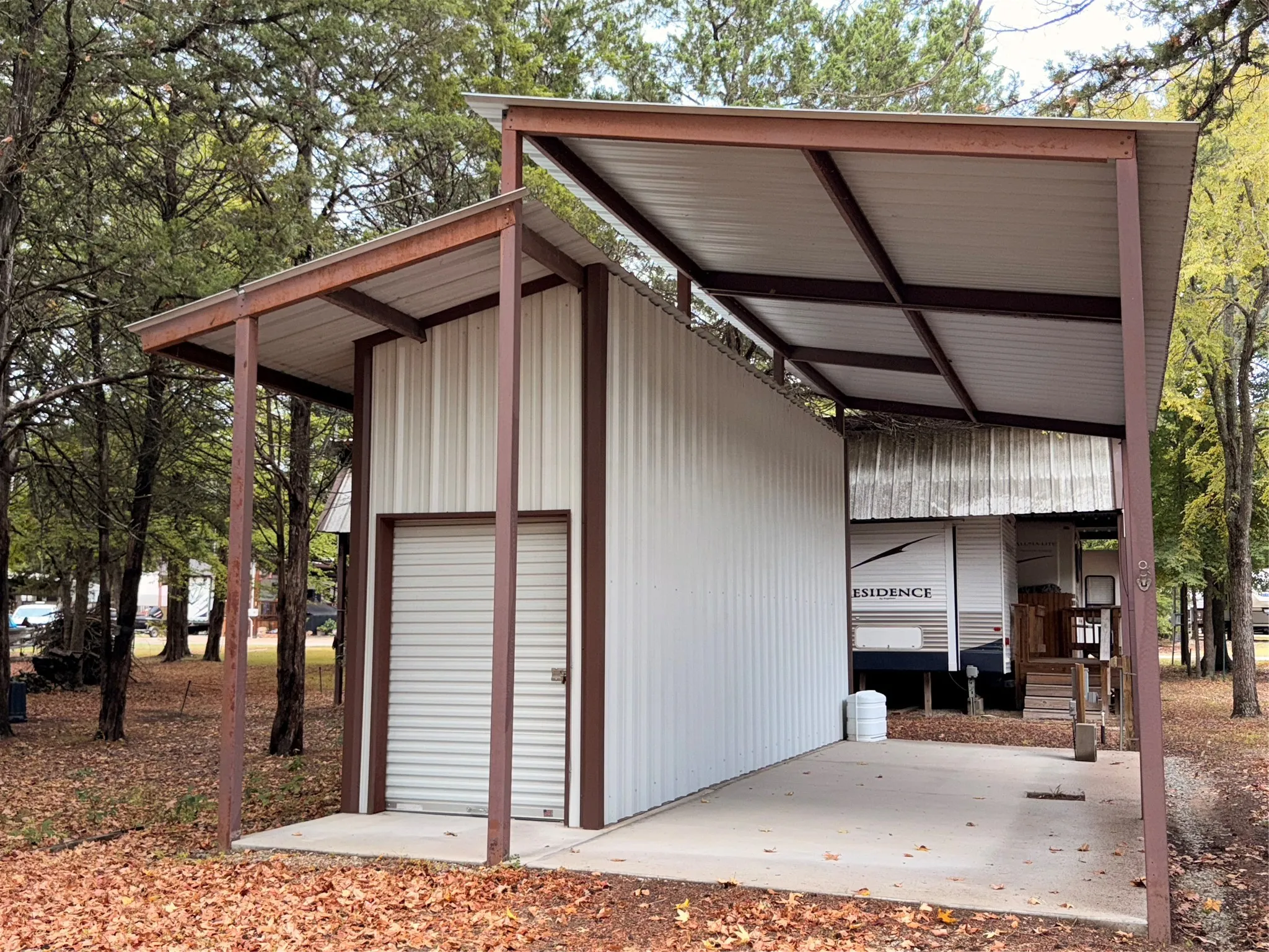 Metal storage structure featuring a roll-up door, an attached open-air carport, and a concrete pad