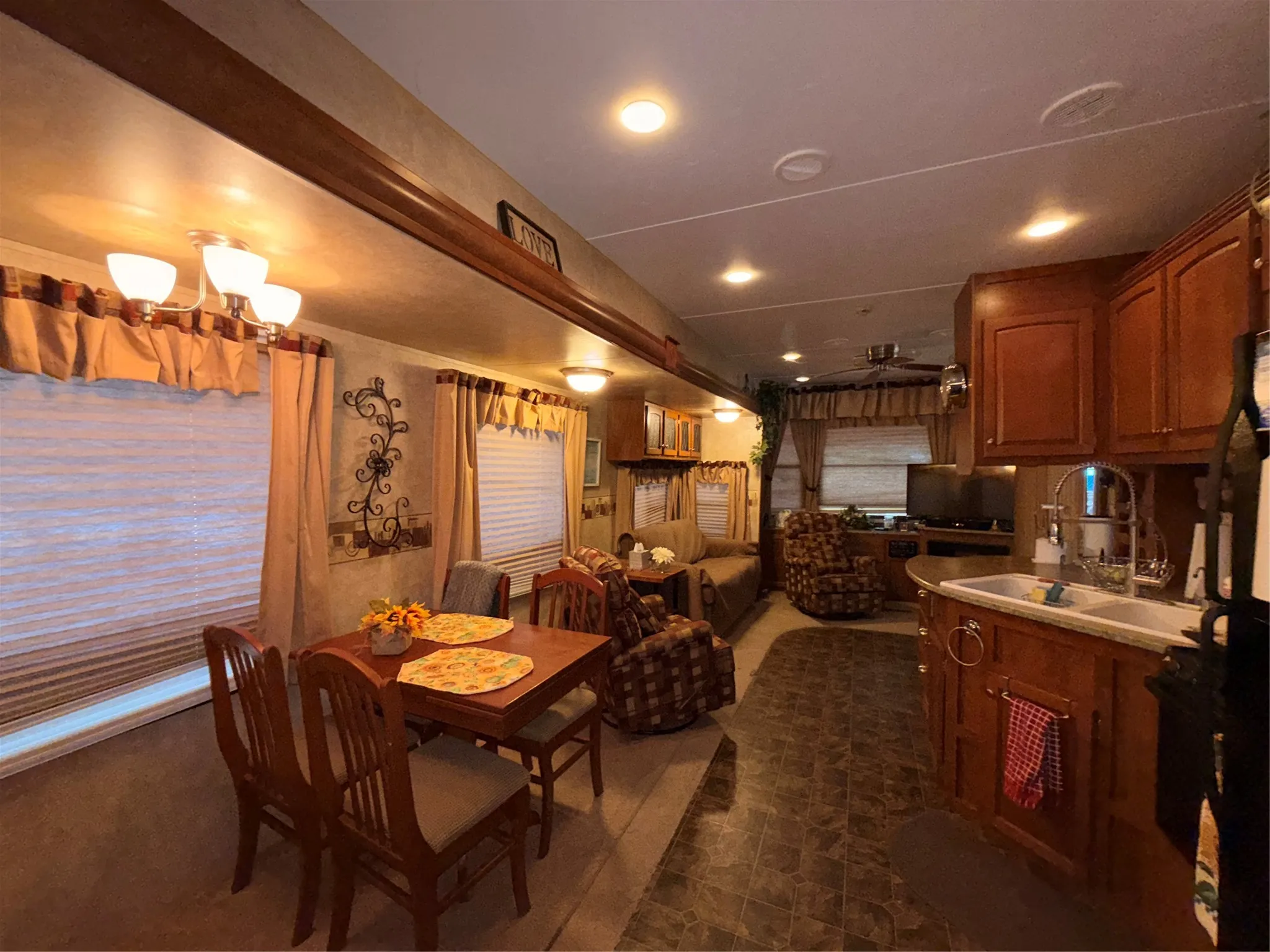 Wood-finish cabinetry, built-in dining table with seating, recessed lighting, and a double basin kitchen sink with gooseneck faucet