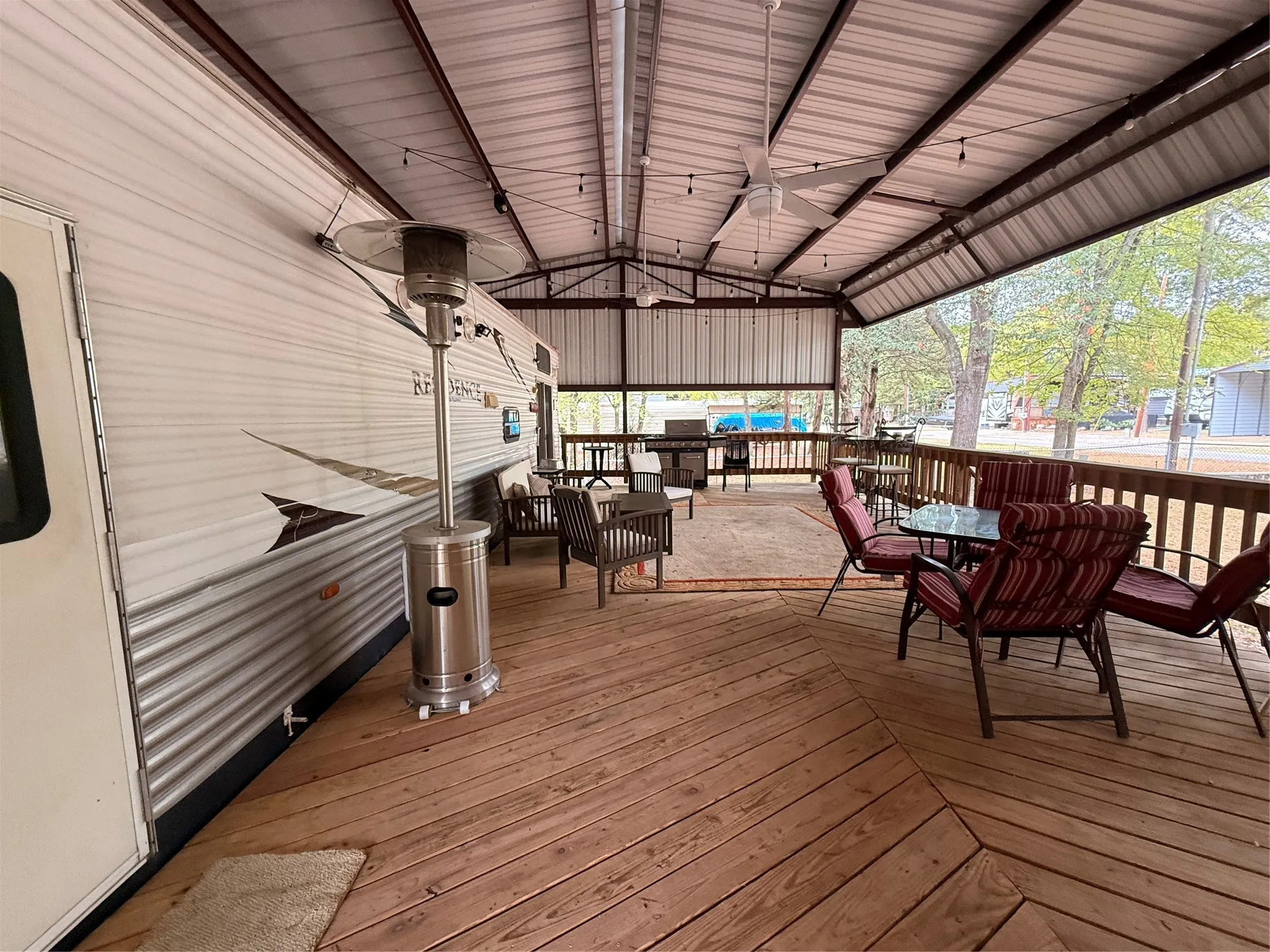 Expansive wooden deck with a durable metal roof structure, featuring multiple ceiling fans and string lighting