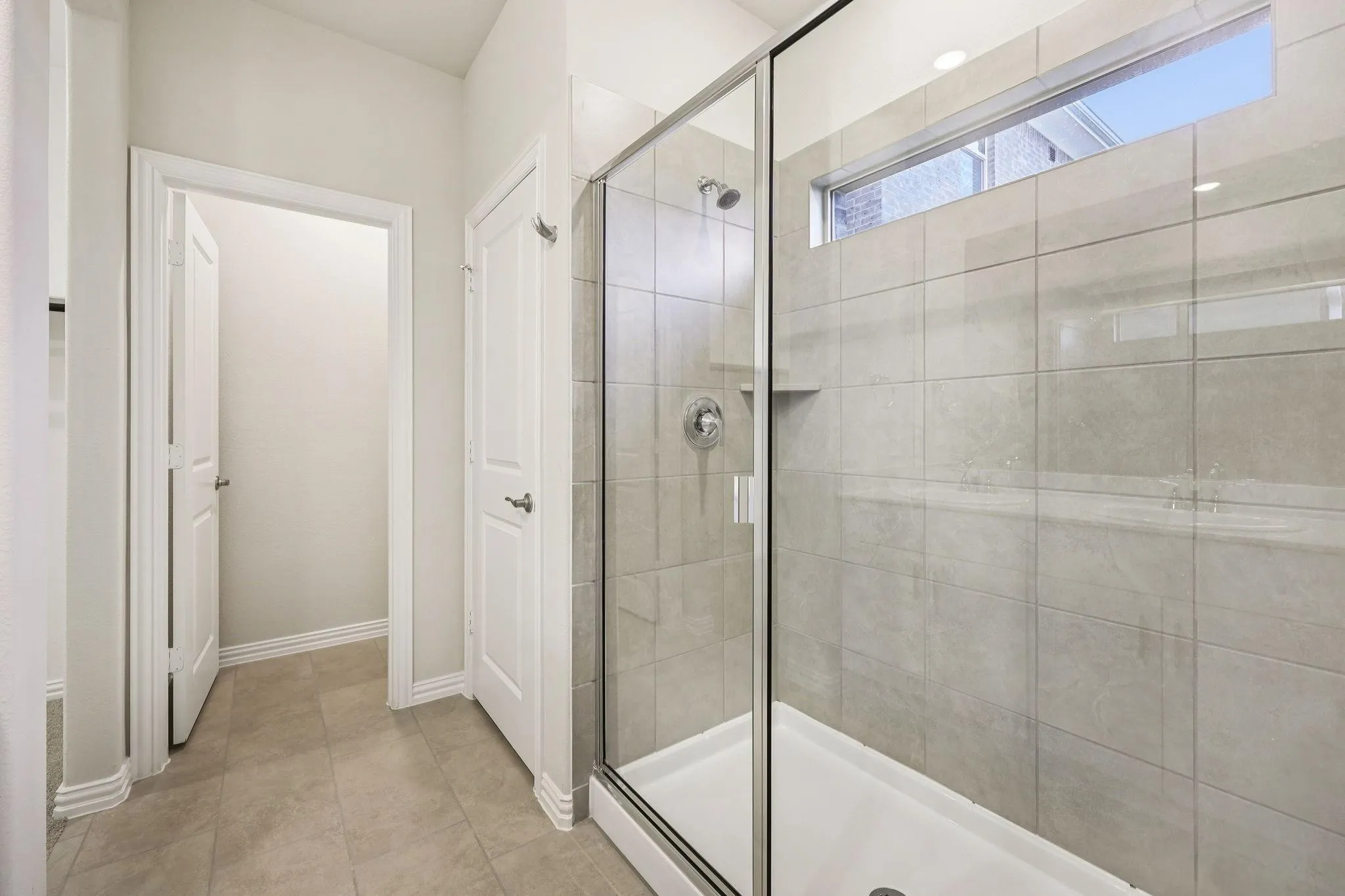 Glass-enclosed shower with tile surround, built-in shelf, and transom window