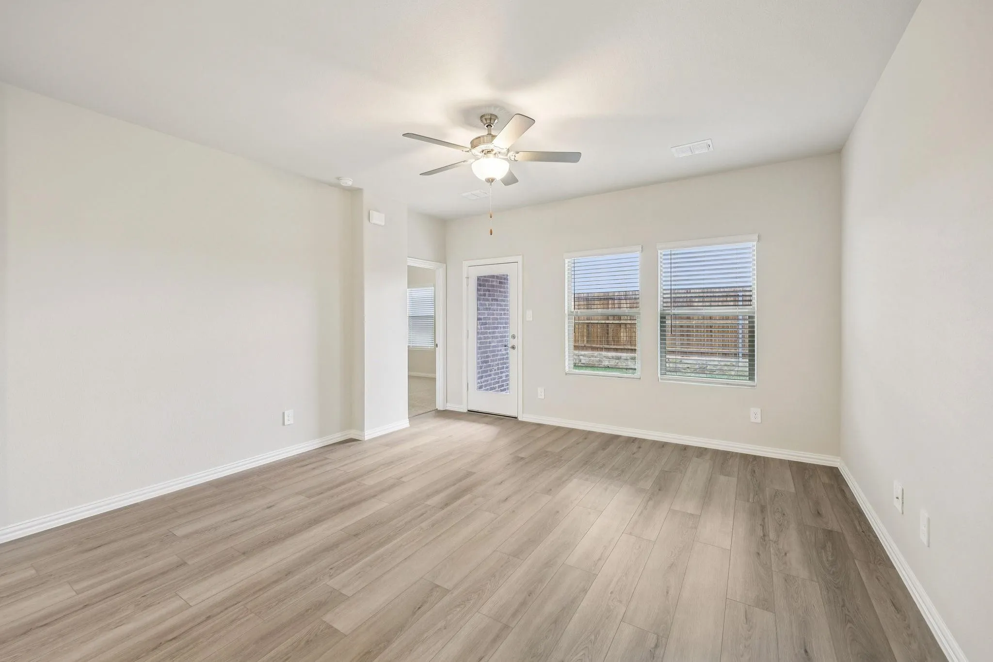 Spacious room featuring wood-finish flooring, neutral paint, a ceiling fan, and multiple windows with blinds
