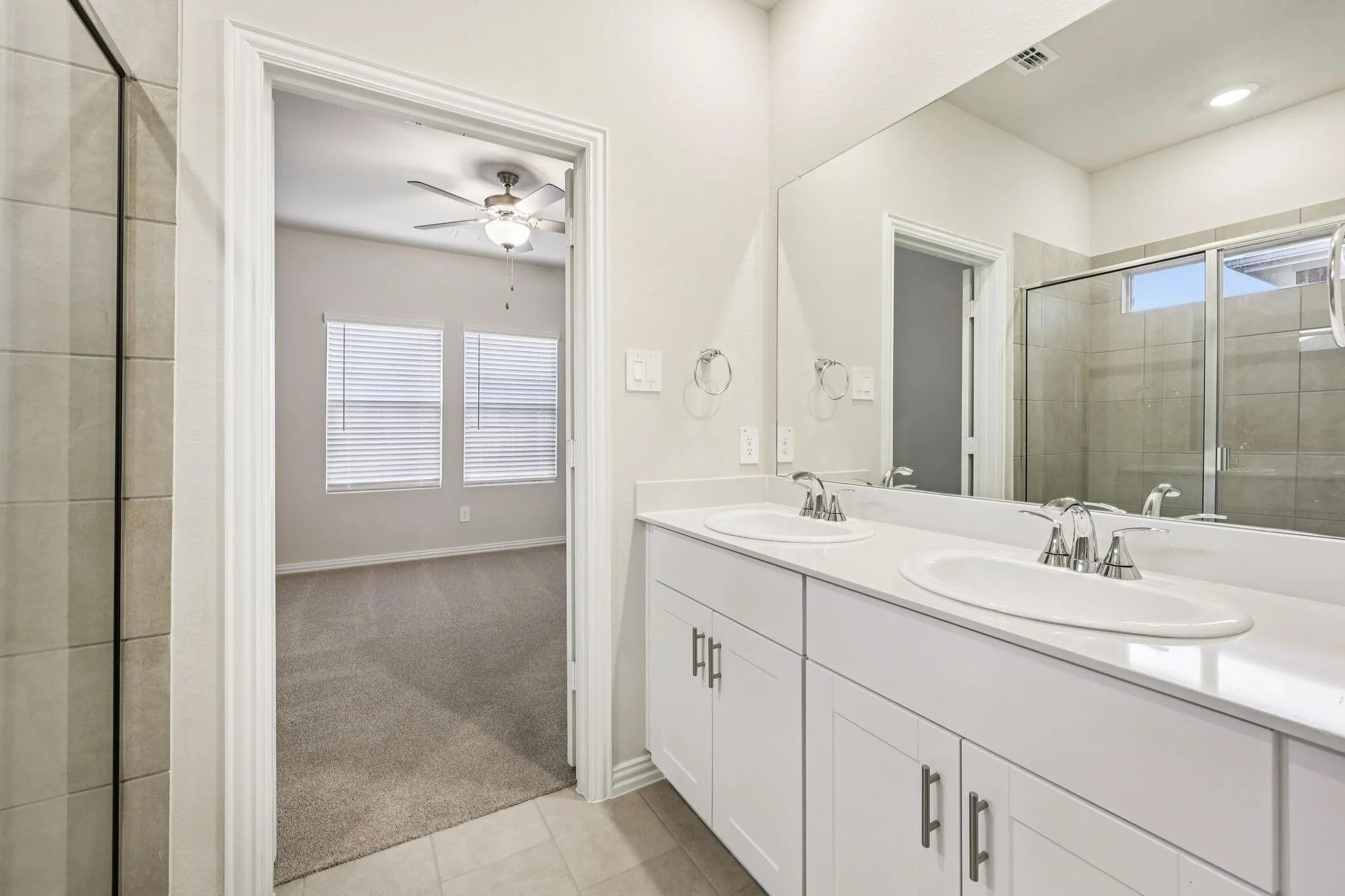 Dual vanity with white cabinetry and integrated sinks, a framed glass shower enclosure, and neutral tile flooring