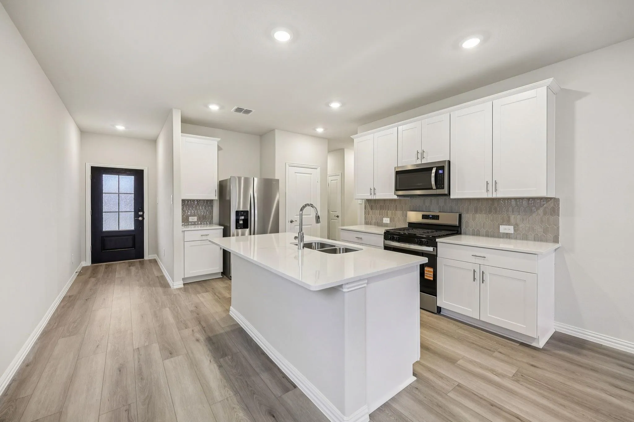 Kitchen featuring an island with an integrated sink, white cabinetry, stainless steel appliances, light-toned flooring, and recessed lighting