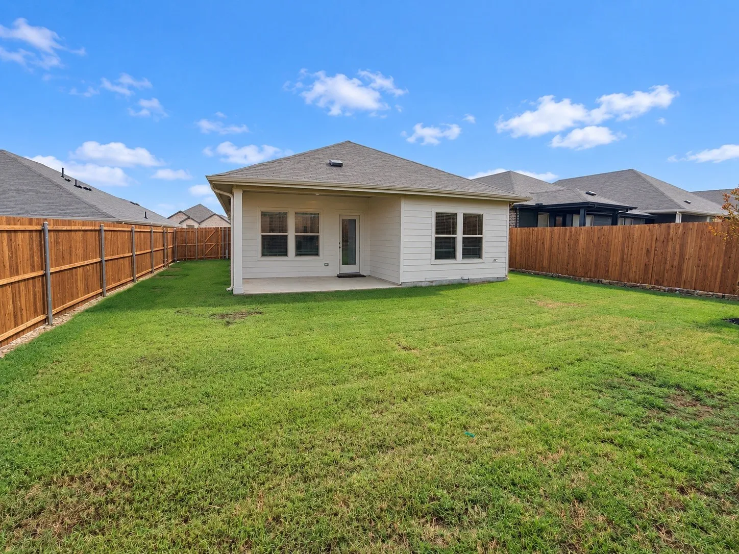 Expansive rear yard featuring green lawn, privacy fencing, and a concrete patio