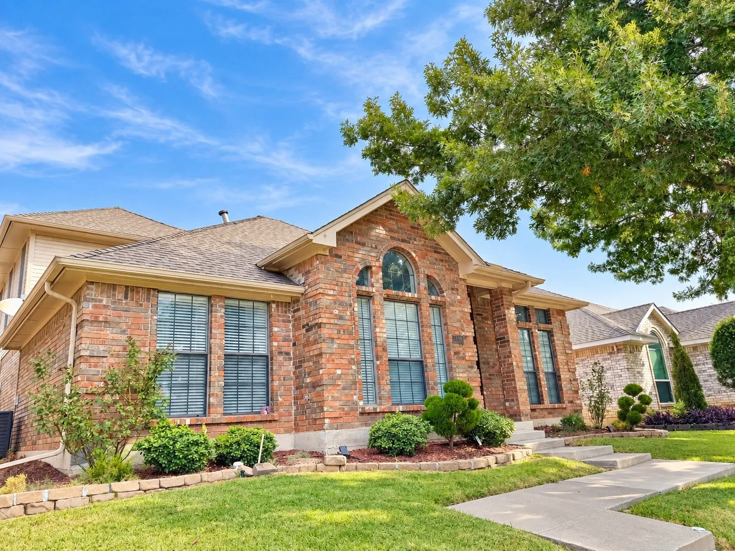 Brick facade with arched window details, multi-level roofline, and established landscaping