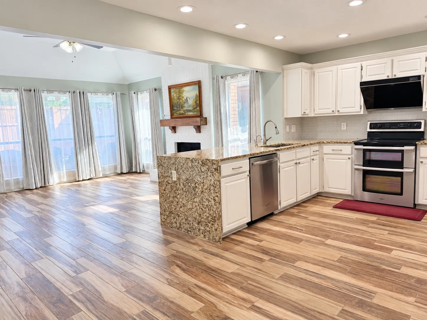 Open-concept living space with wood-finish flooring, white cabinetry, stainless steel appliances, and a fireplace feature