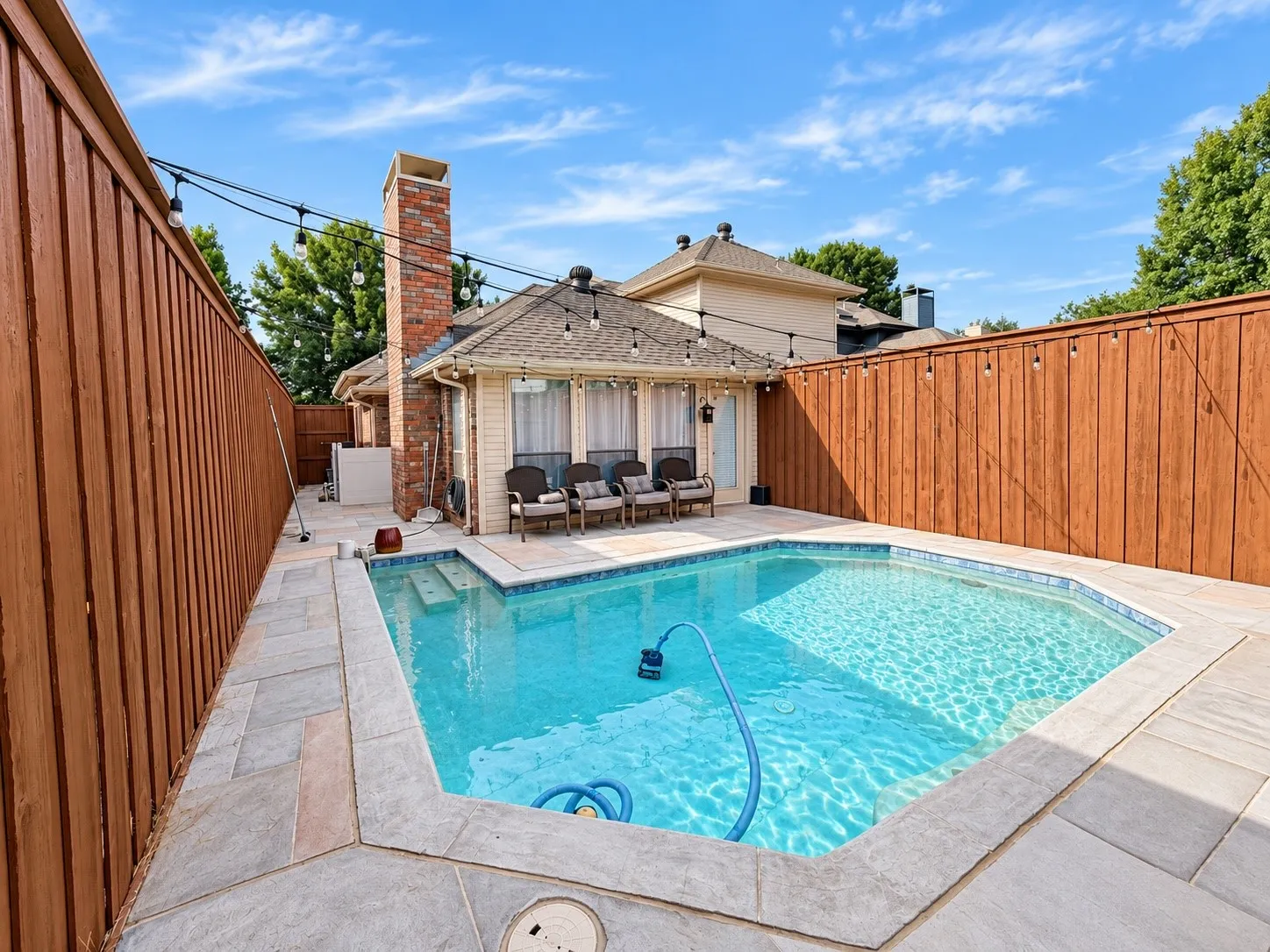Outdoor pool with surrounding stone patio, wood privacy fencing, and string lighting