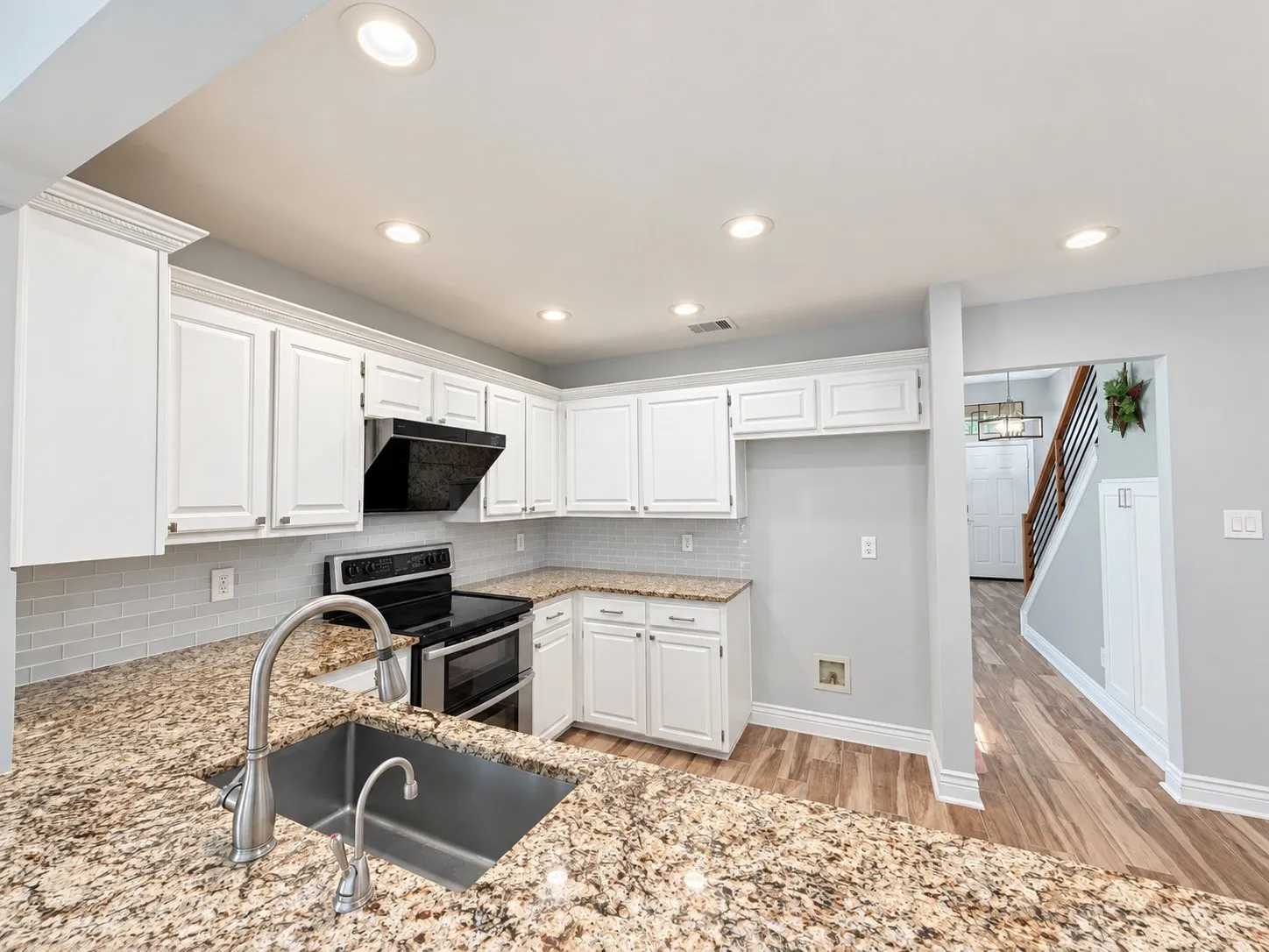 Kitchen featuring white cabinetry, granite countertops, stainless steel sink with pull-down faucet, tile backsplash, and recessed lighting