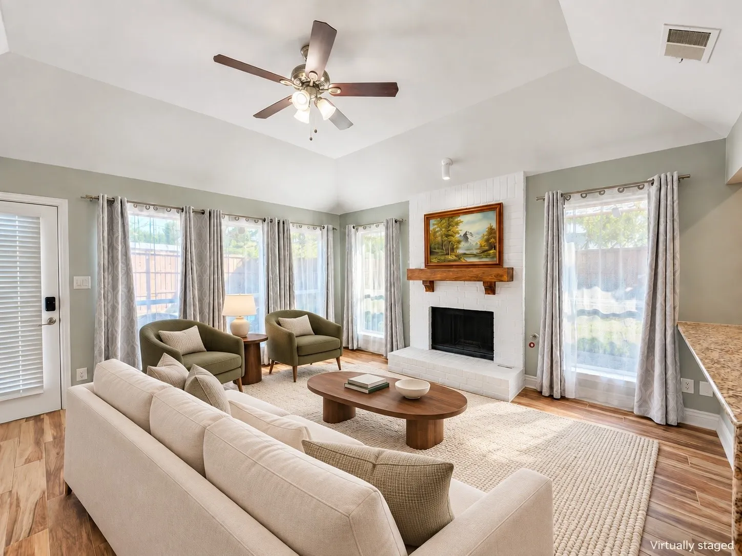 Vaulted ceiling with a ceiling fan, a white brick fireplace with a wood mantle, wood-finish flooring, and multiple windows
