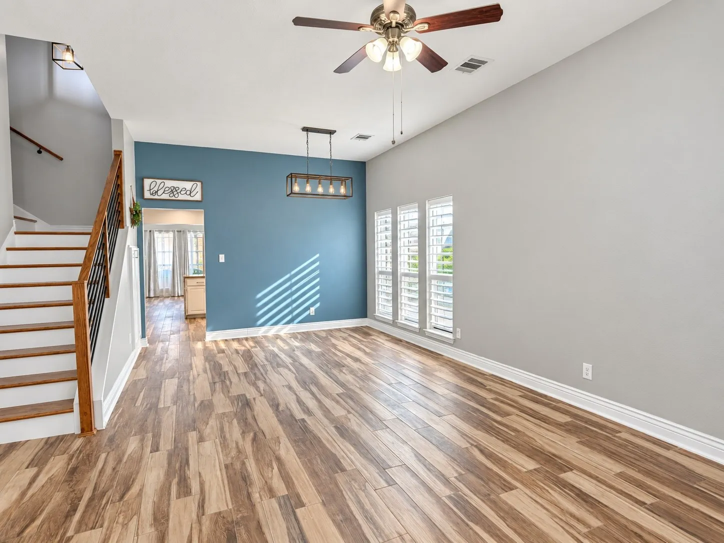 Vaulted ceiling with a ceiling fan, wood-finish flooring, staircase with wood steps and black metal balusters, and multiple windows with plantation shutters