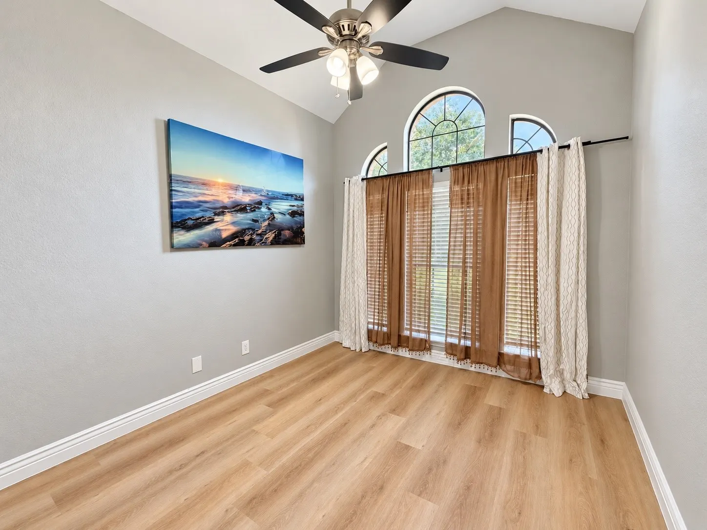 Vaulted ceiling, wood-finish flooring, ceiling fan, and arched windows