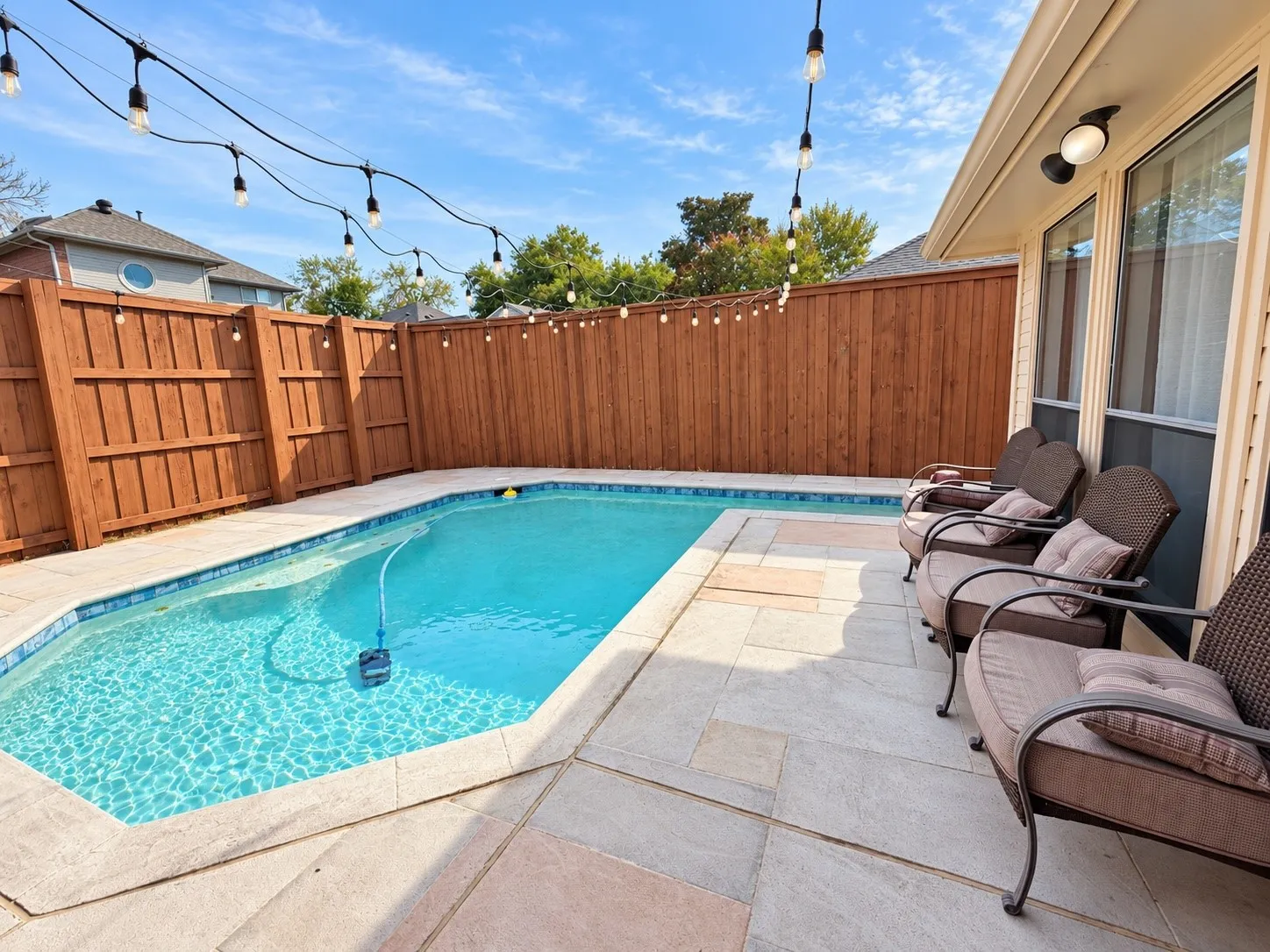 Private backyard featuring a rectangular swimming pool, light-toned patio pavers, and wood privacy fencing