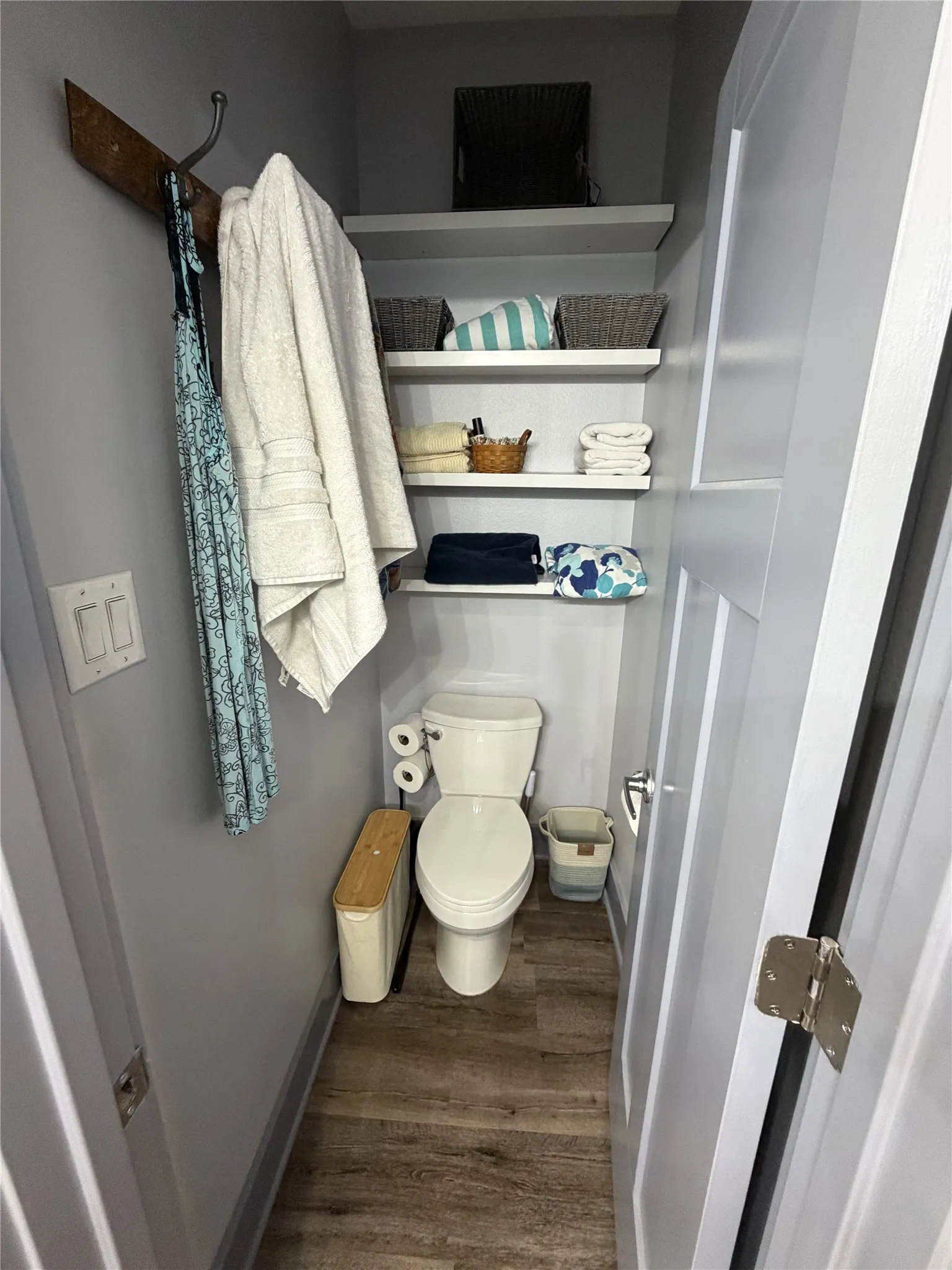 Wood-finish flooring with a white toilet and white floating shelves
