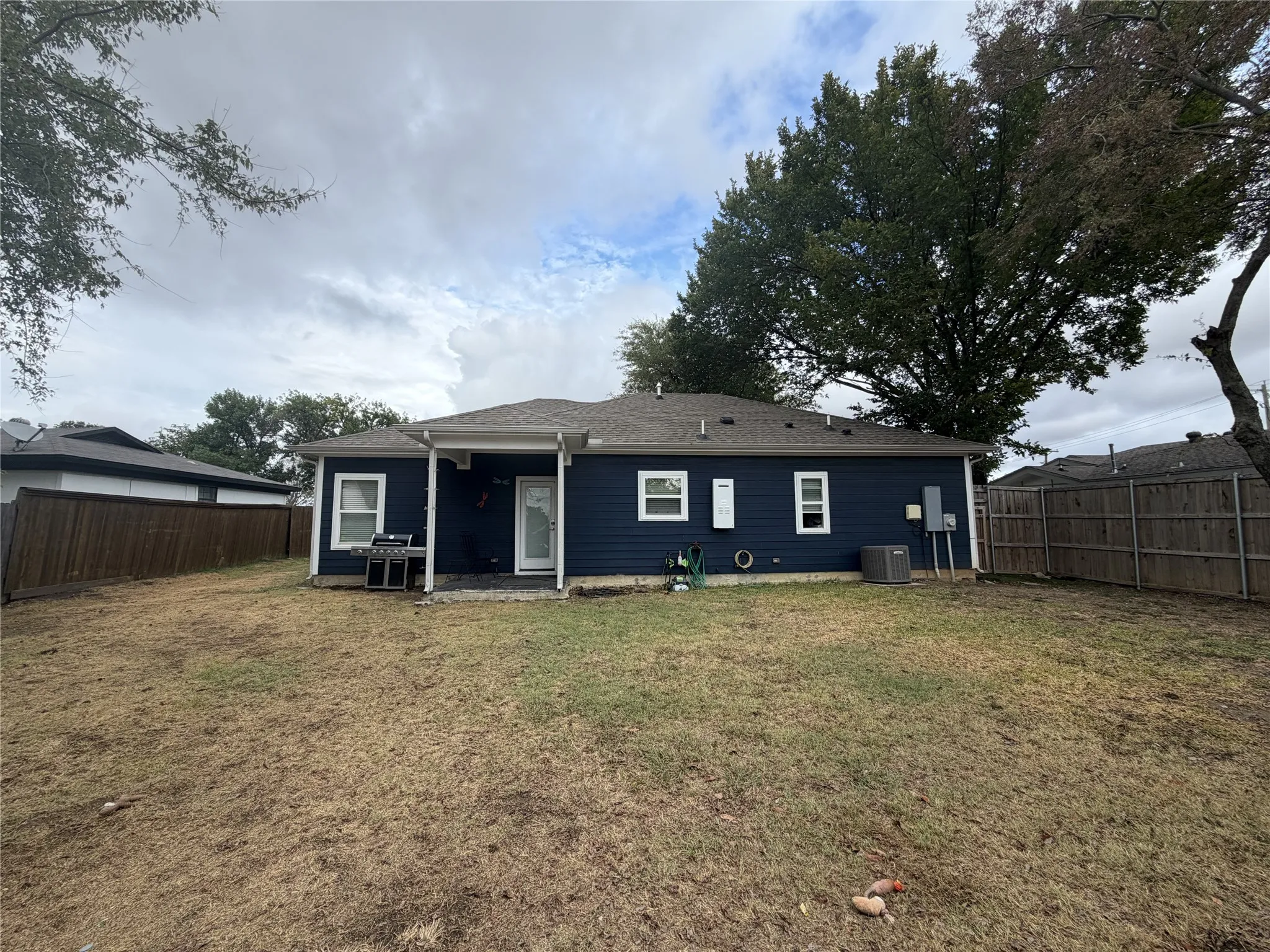 Exterior featuring dark blue siding, white trim windows, a covered patio, and a wood privacy fence