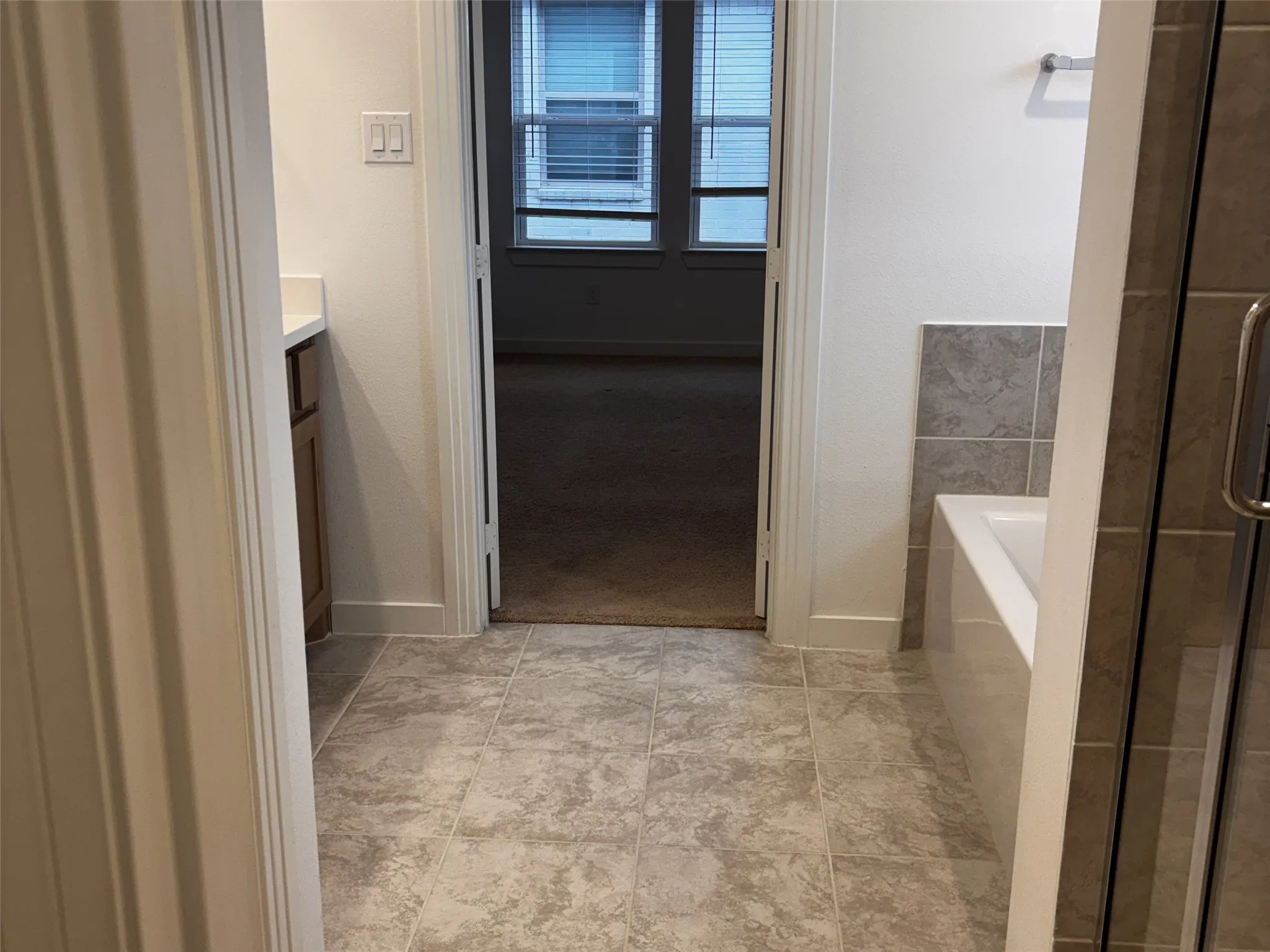 Tile flooring, built-in bathtub with tiled surround, glass-enclosed shower, single vanity with countertop, wood-finish cabinetry