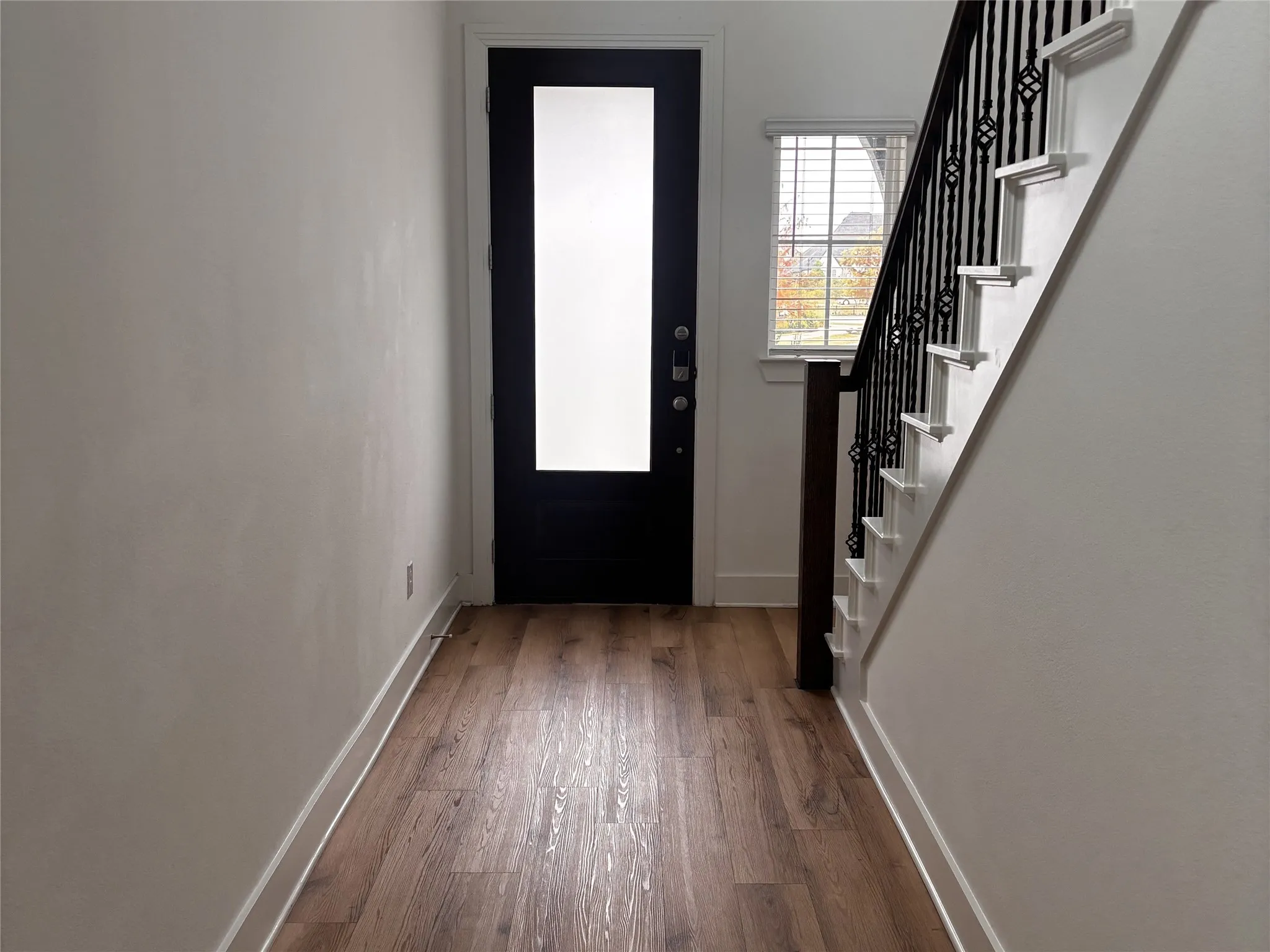 Entryway featuring wood-finish flooring, a dark-paneled door with frosted glass, and a staircase with decorative metal balusters and a wood handrail