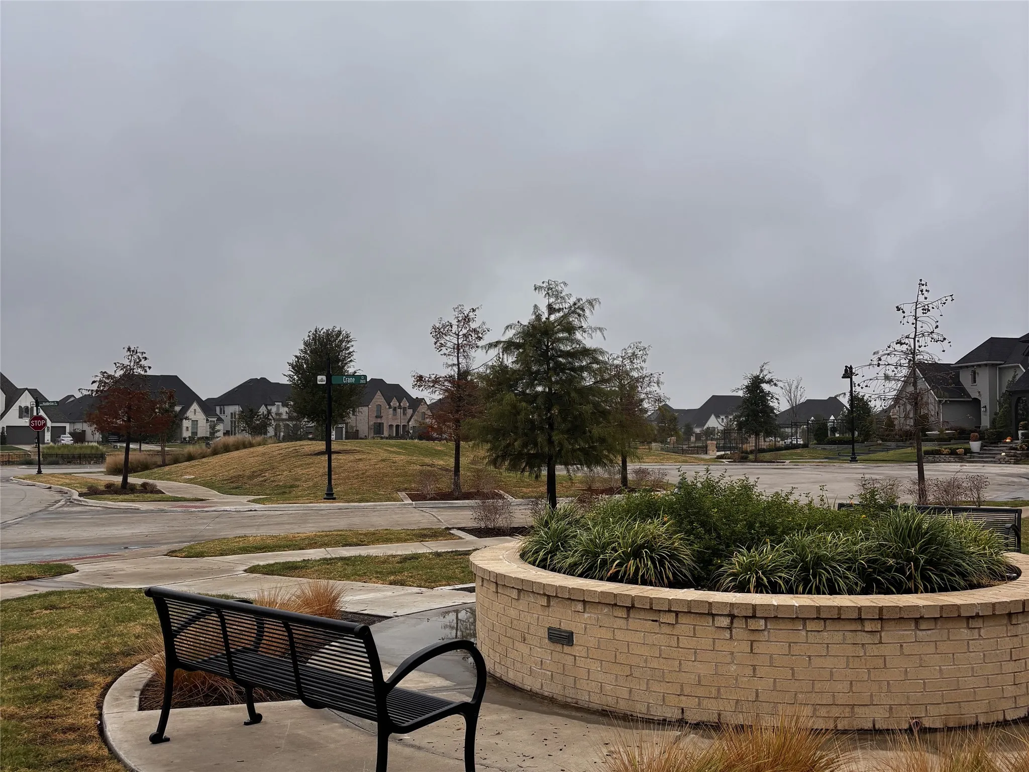 Community greenspace featuring a decorative brick planter, mature trees, and paved walkways
