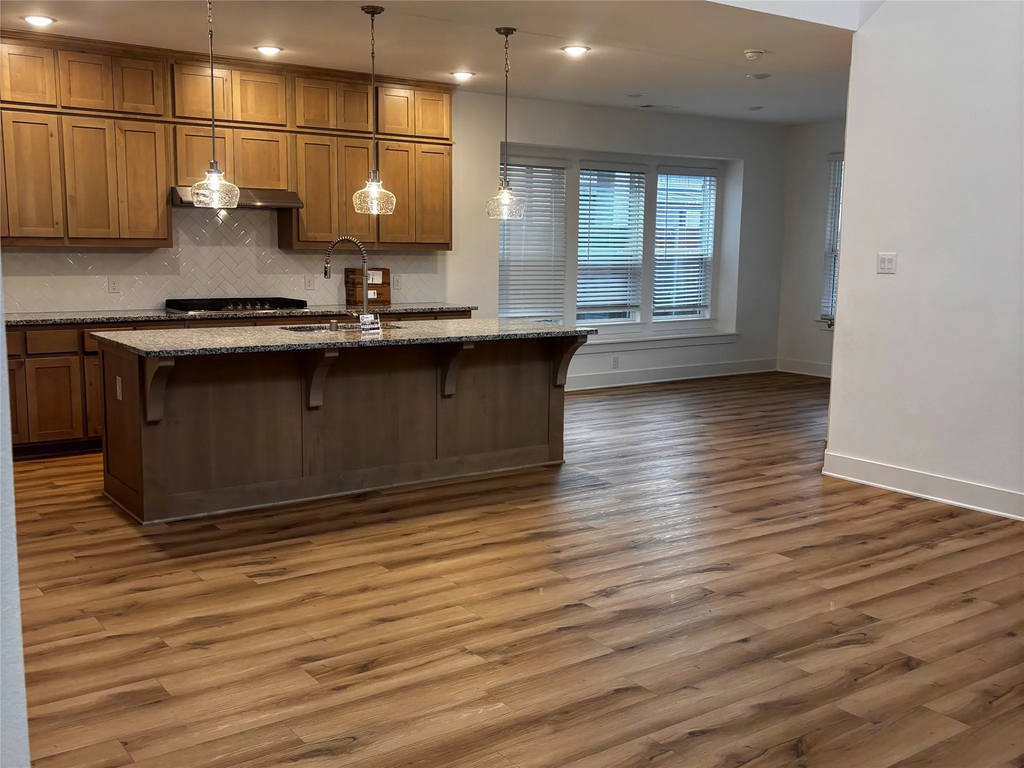 Kitchen featuring wood cabinetry, granite countertops, tile backsplash, and a central island with a sink