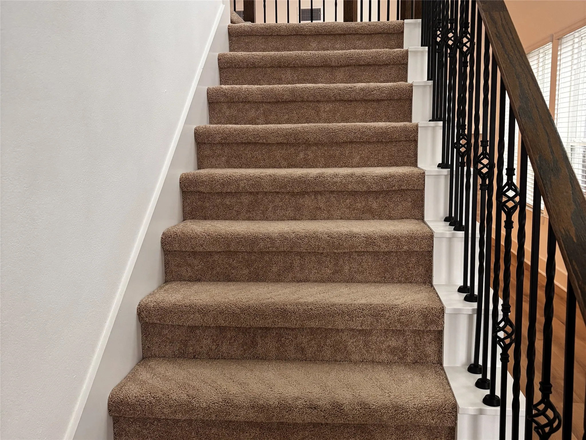 Staircase with carpeted treads, white risers, and wrought iron balusters featuring decorative accents