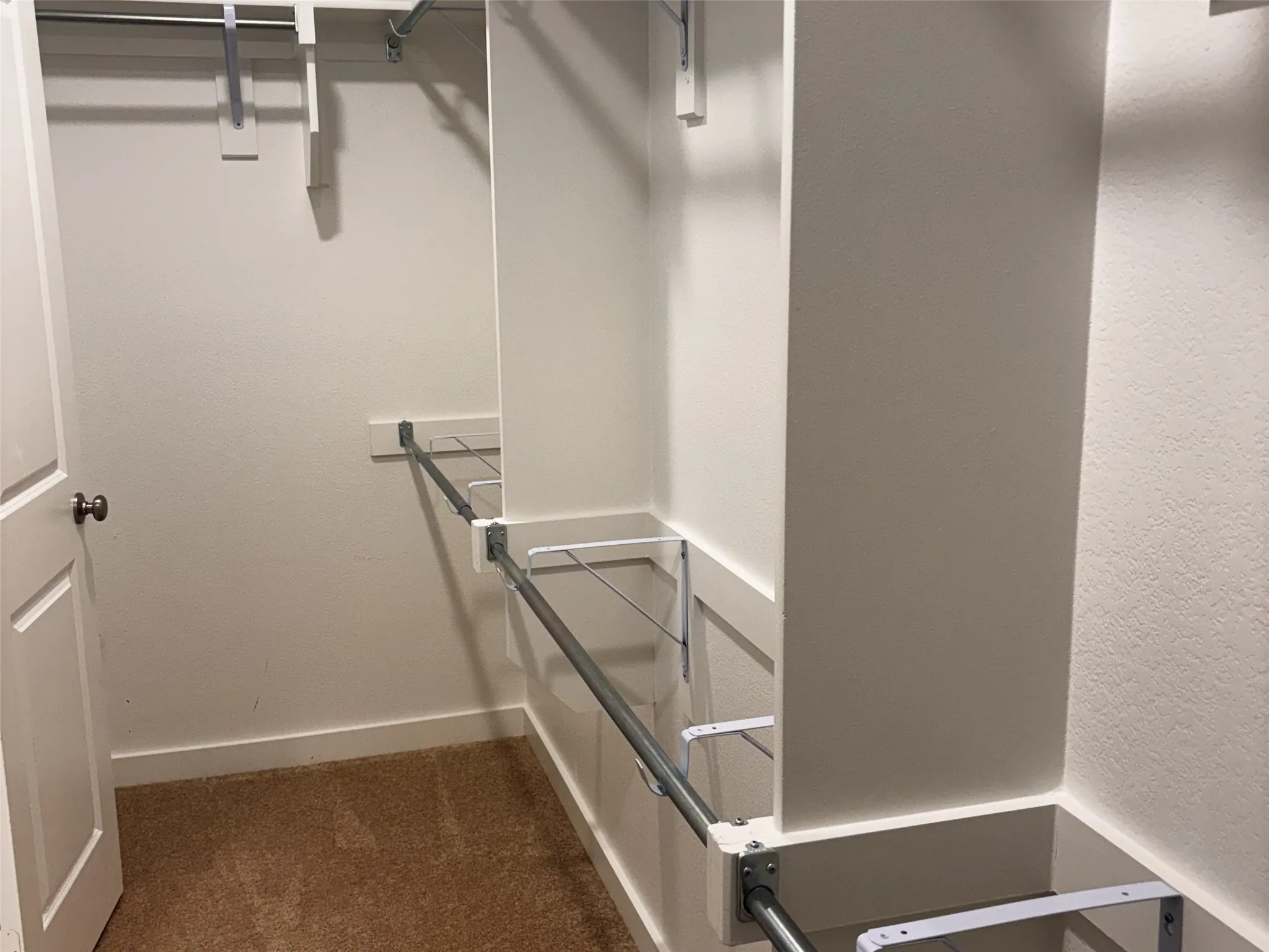 Walk-in closet with carpet flooring, white walls, and built-in metal shelving and hanging rods