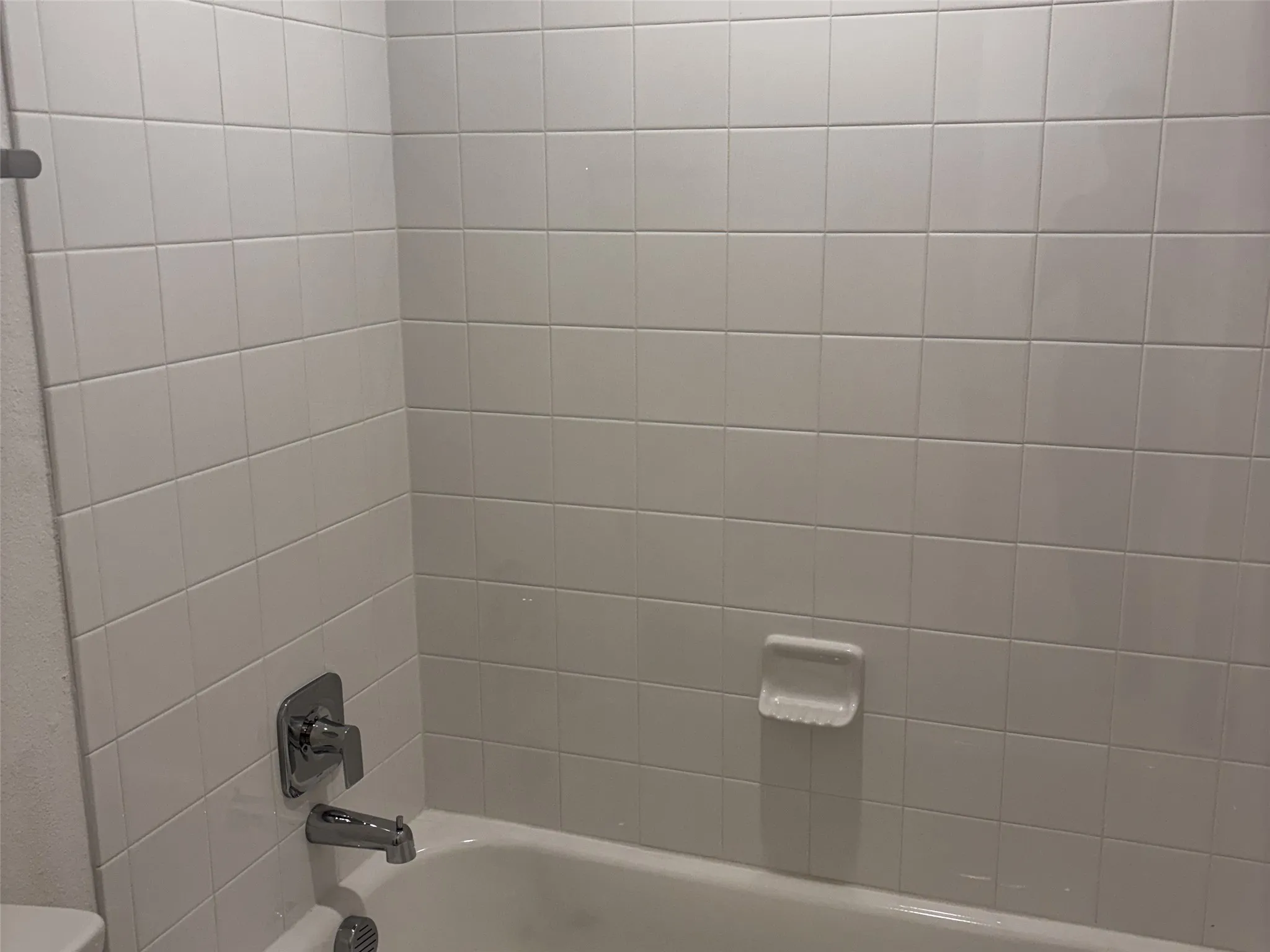 Bathtub with white tile surround, chrome fixtures, and built-in soap dish