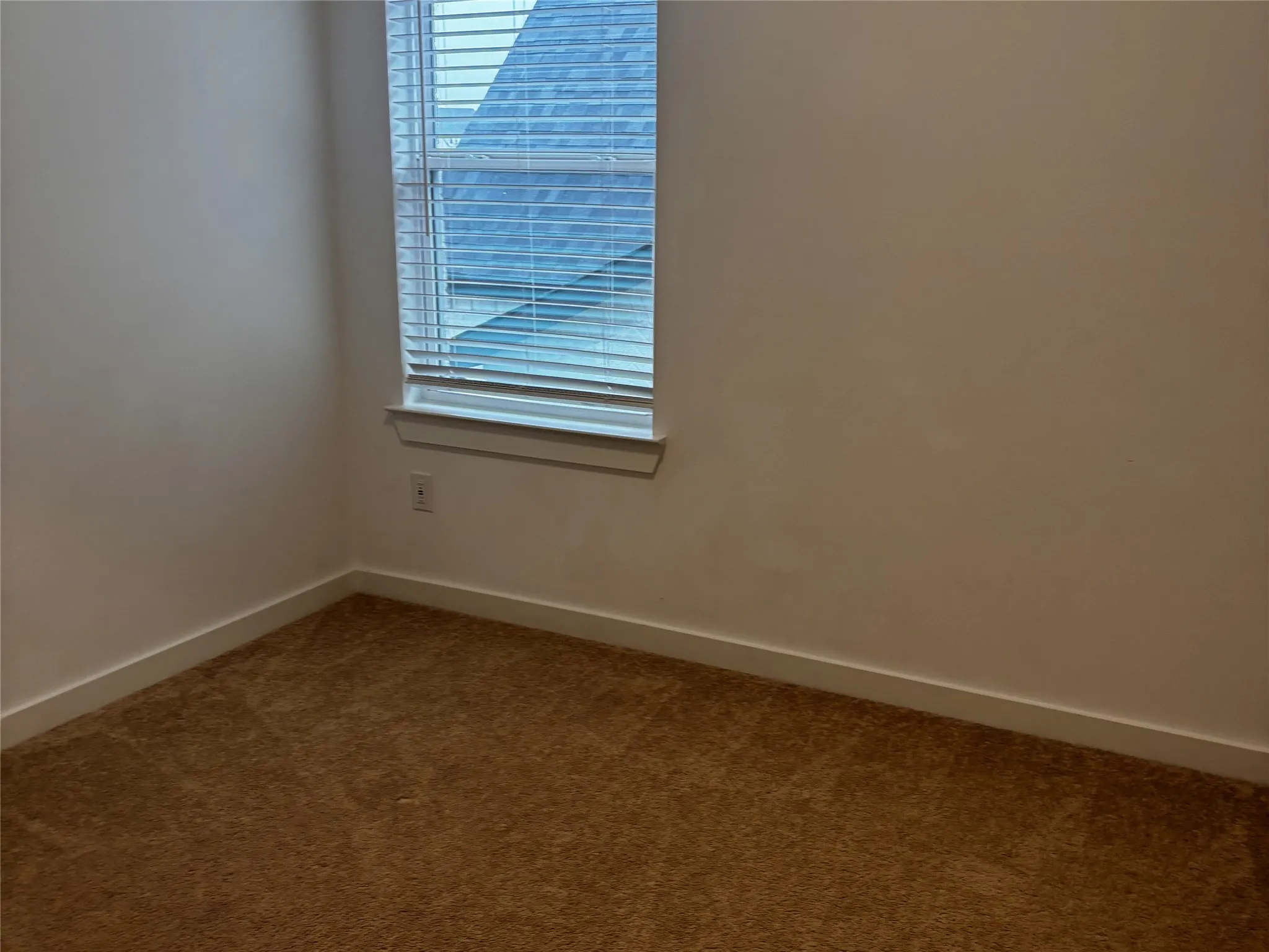 Neutral-toned walls, a window with horizontal blinds, and a brown carpeted floor