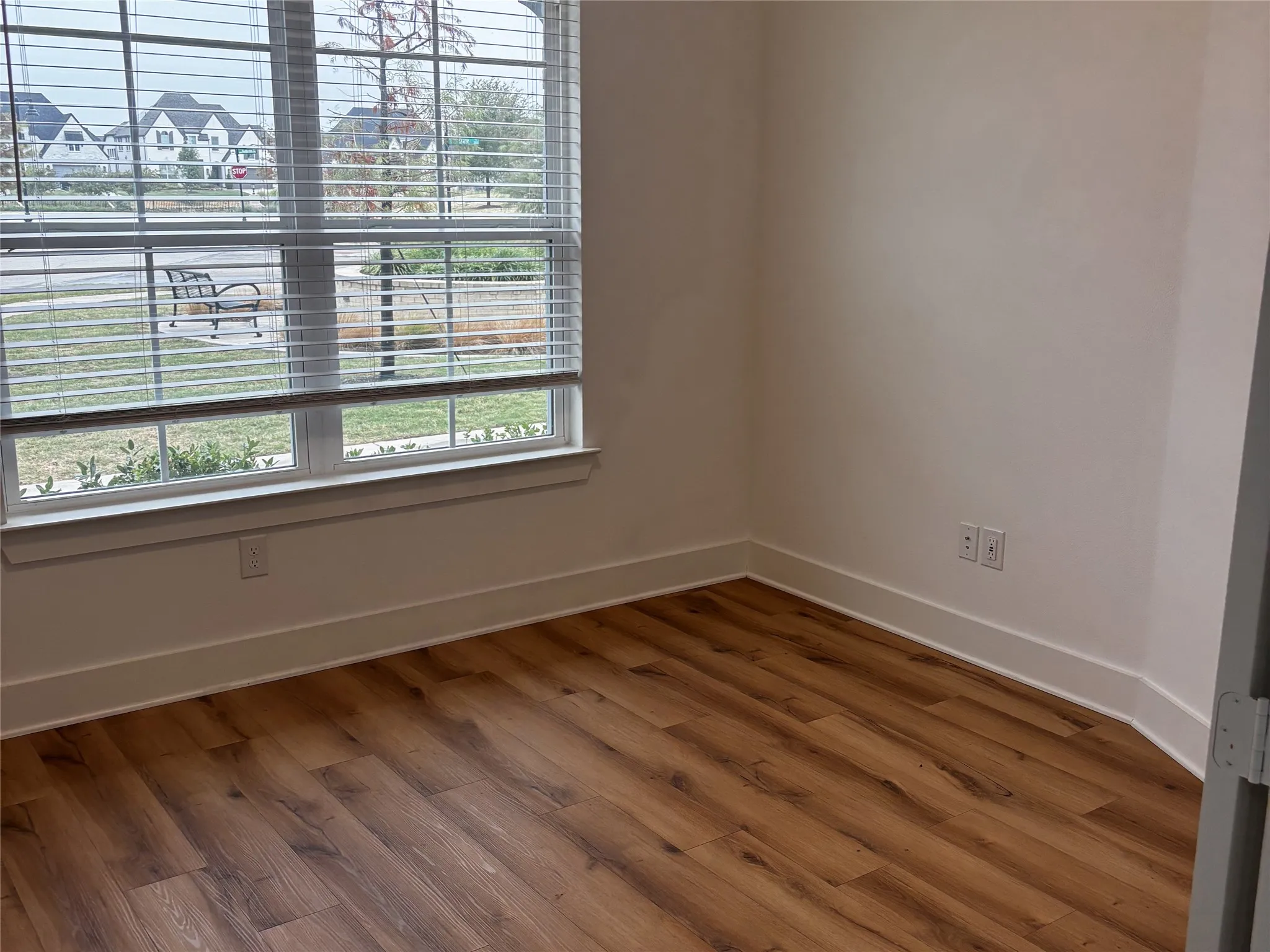 Wood-finish flooring, white wall paint, window with horizontal blinds, white window trim