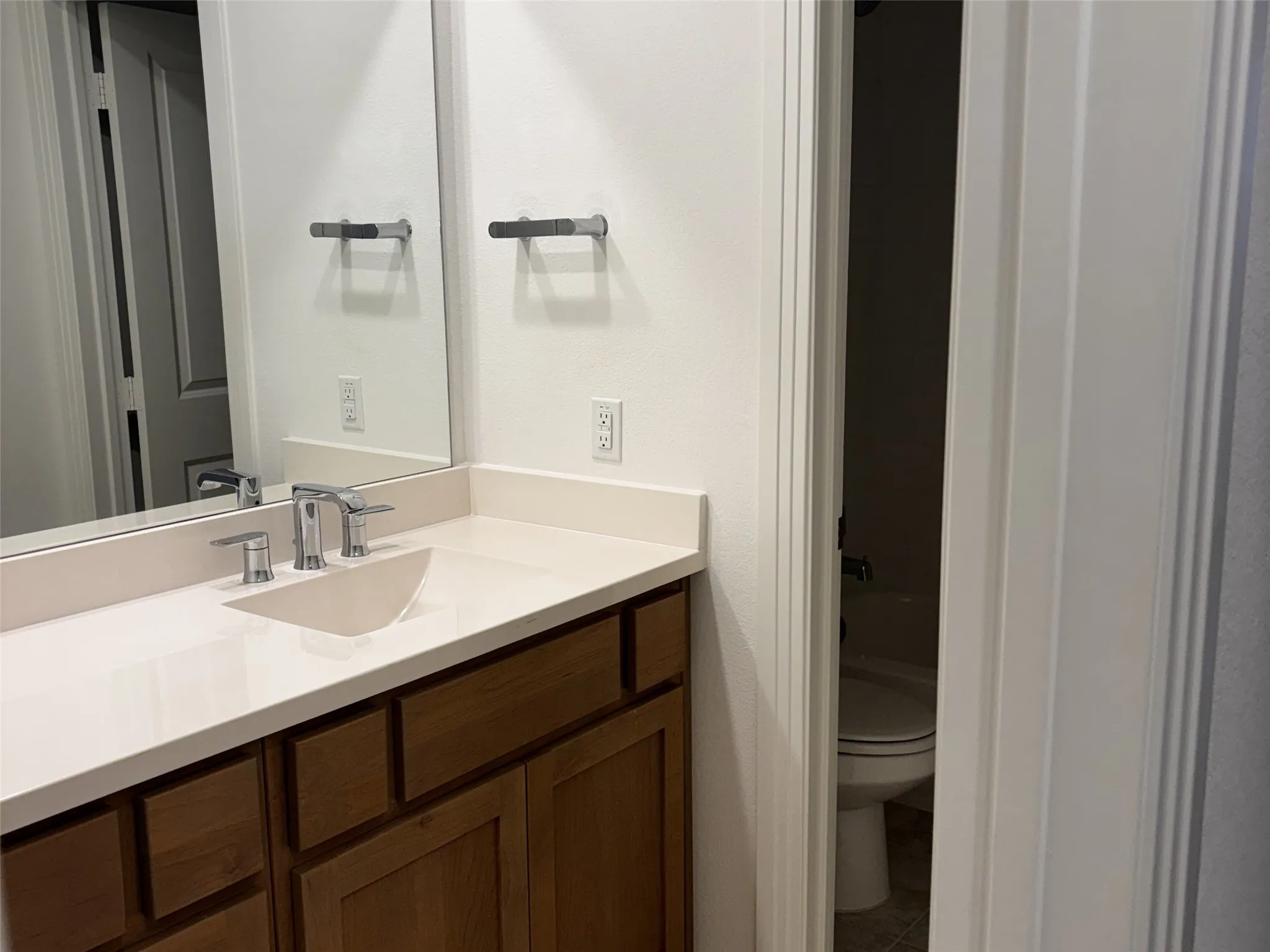 Vanity with wood-finish cabinetry, light-toned countertop, and undermount sink with chrome-finish faucet