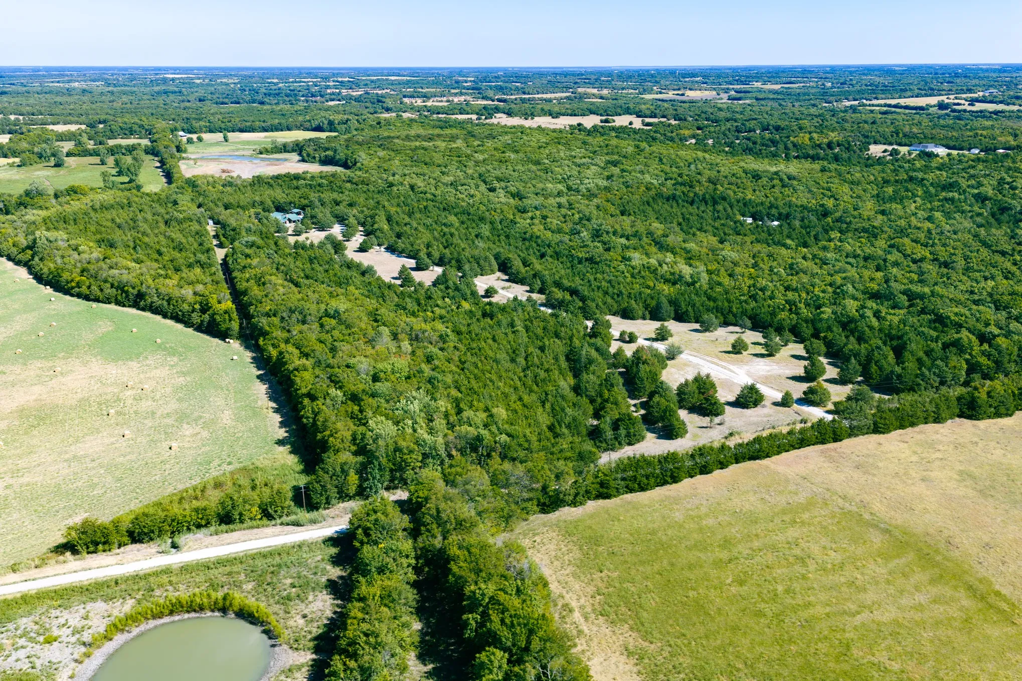 Expansive land featuring wooded areas, open fields, and a private pond