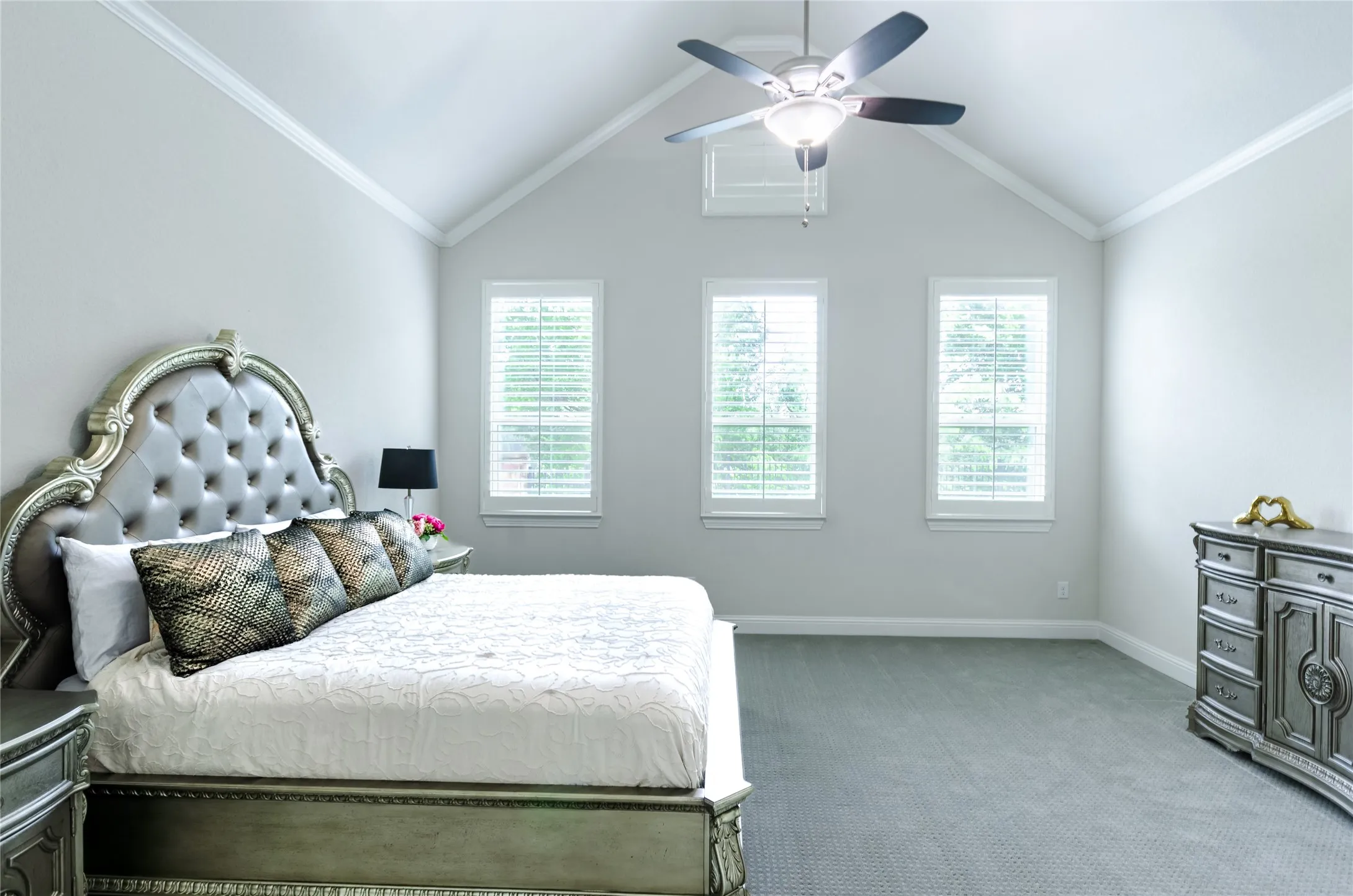 Vaulted ceiling room featuring three windows with plantation shutters, a ceiling fan, crown molding, and grey carpeting