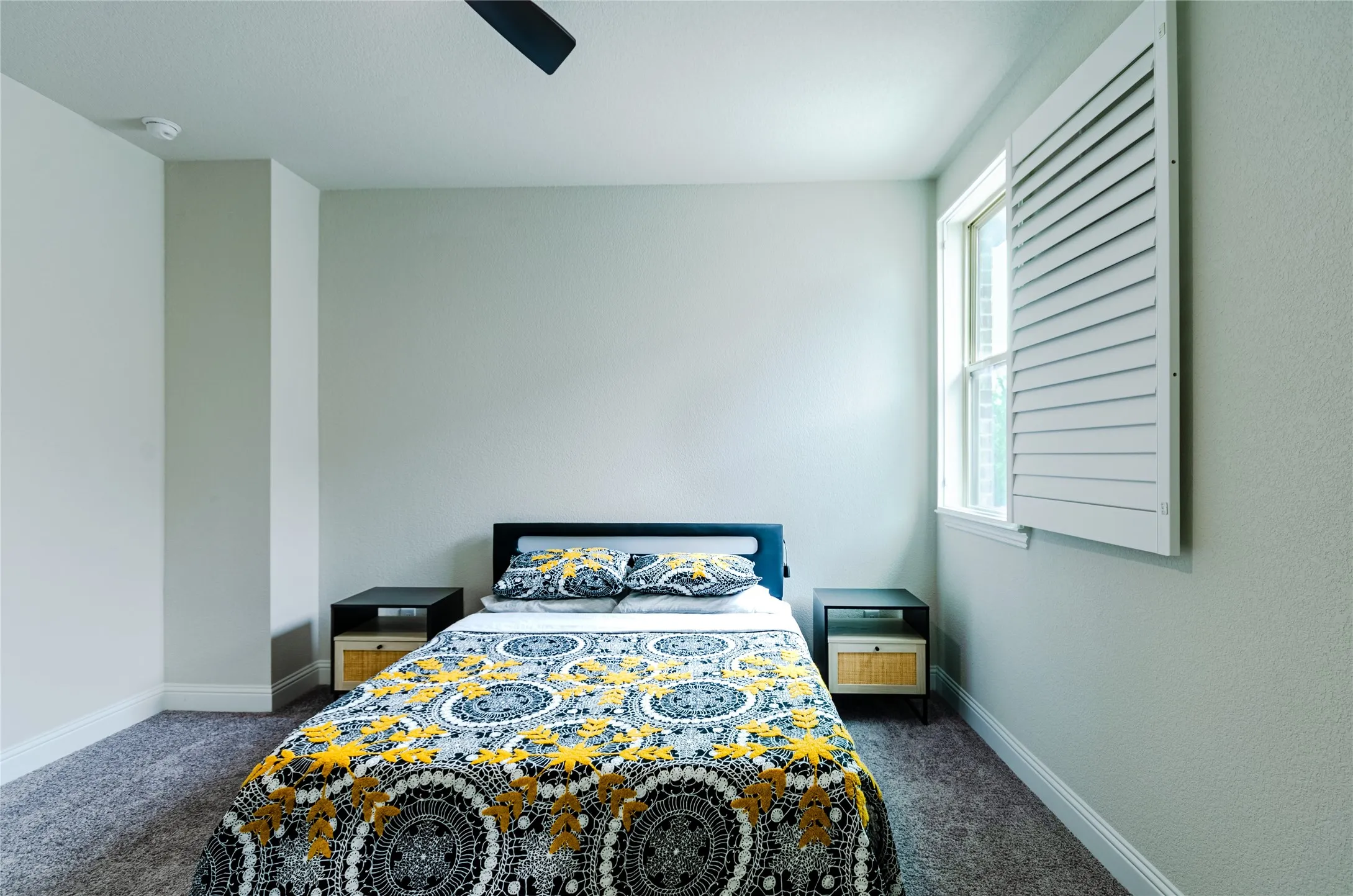 Bedroom featuring neutral wall tones, textured carpeting, a single window with white louvered shutters, ceiling fan, and baseboard molding