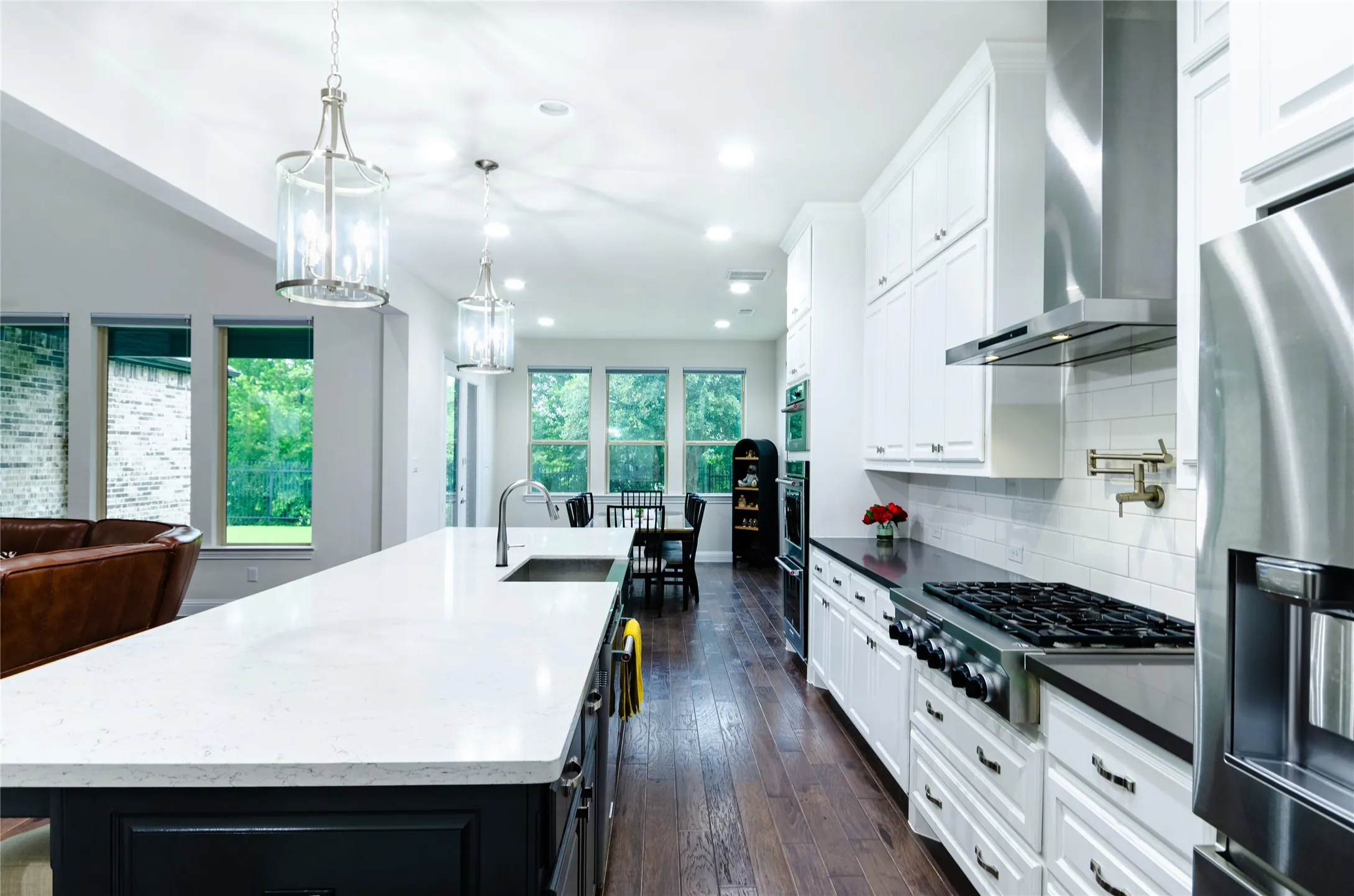 Spacious kitchen featuring an expansive island with an undermount sink, stainless steel appliances, white cabinetry, dark countertops, and wood-finish flooring
