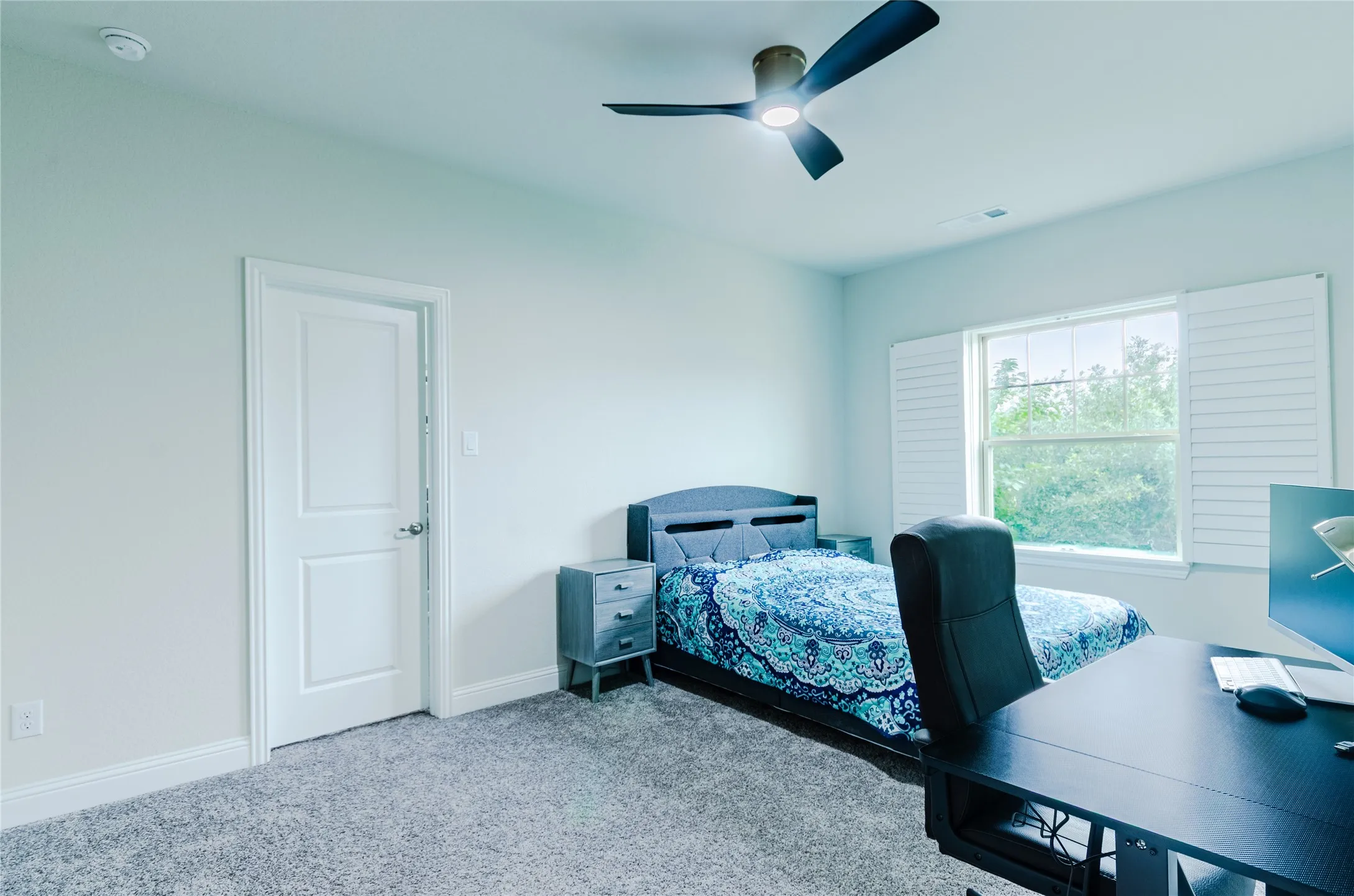 Bedroom featuring light gray carpet, a ceiling fan with integrated lighting, and a window with white louvered shutters