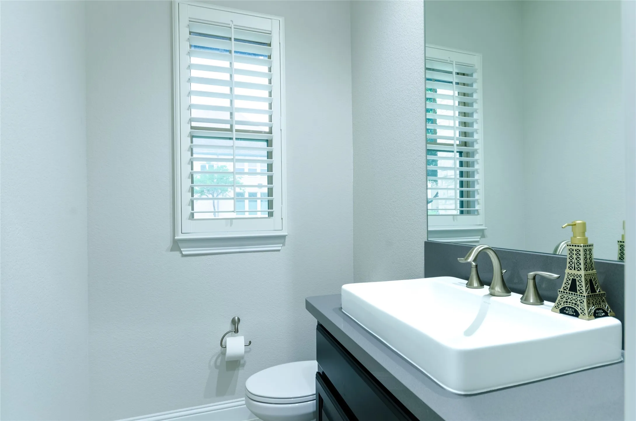 Bathroom with a white vessel sink, brushed nickel faucet, dark vanity, and a window with plantation shutters