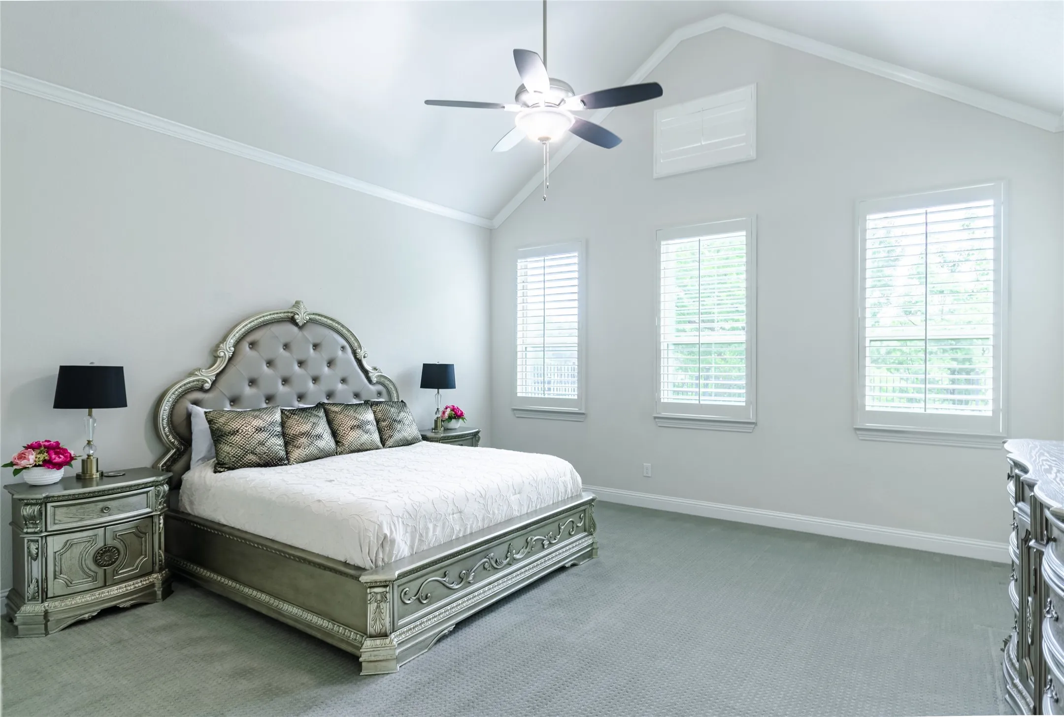 Vaulted ceiling room featuring three windows with plantation shutters, crown molding, and a ceiling fan