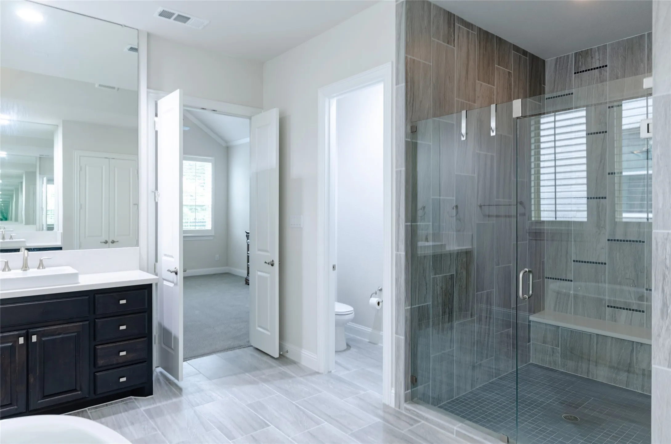 Contemporary bathroom featuring a glass-enclosed shower with a built-in bench, a dark wood-finish vanity with a vessel sink, and large format tile flooring